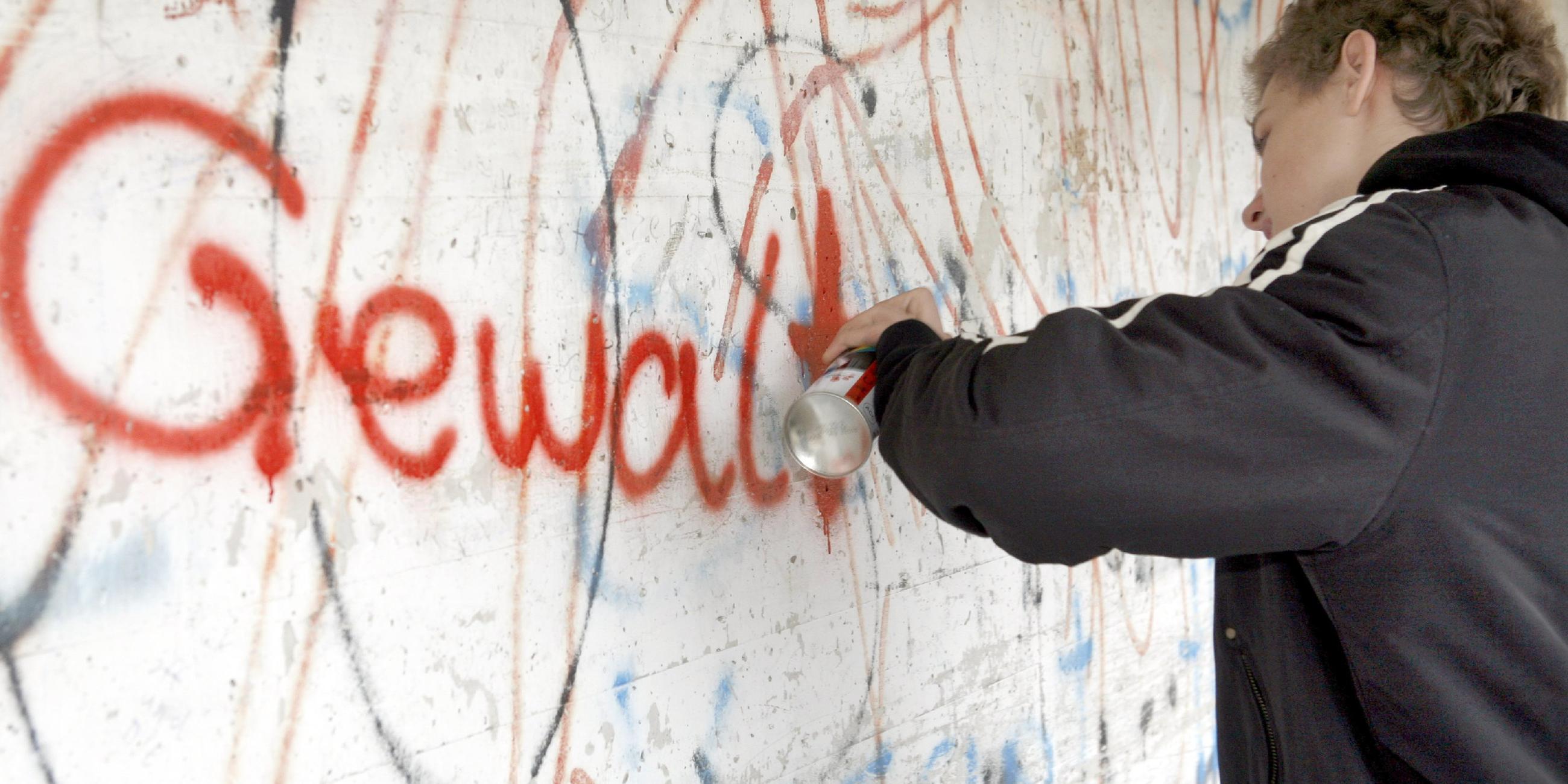 Person sprüht Graffiti an eine Wand