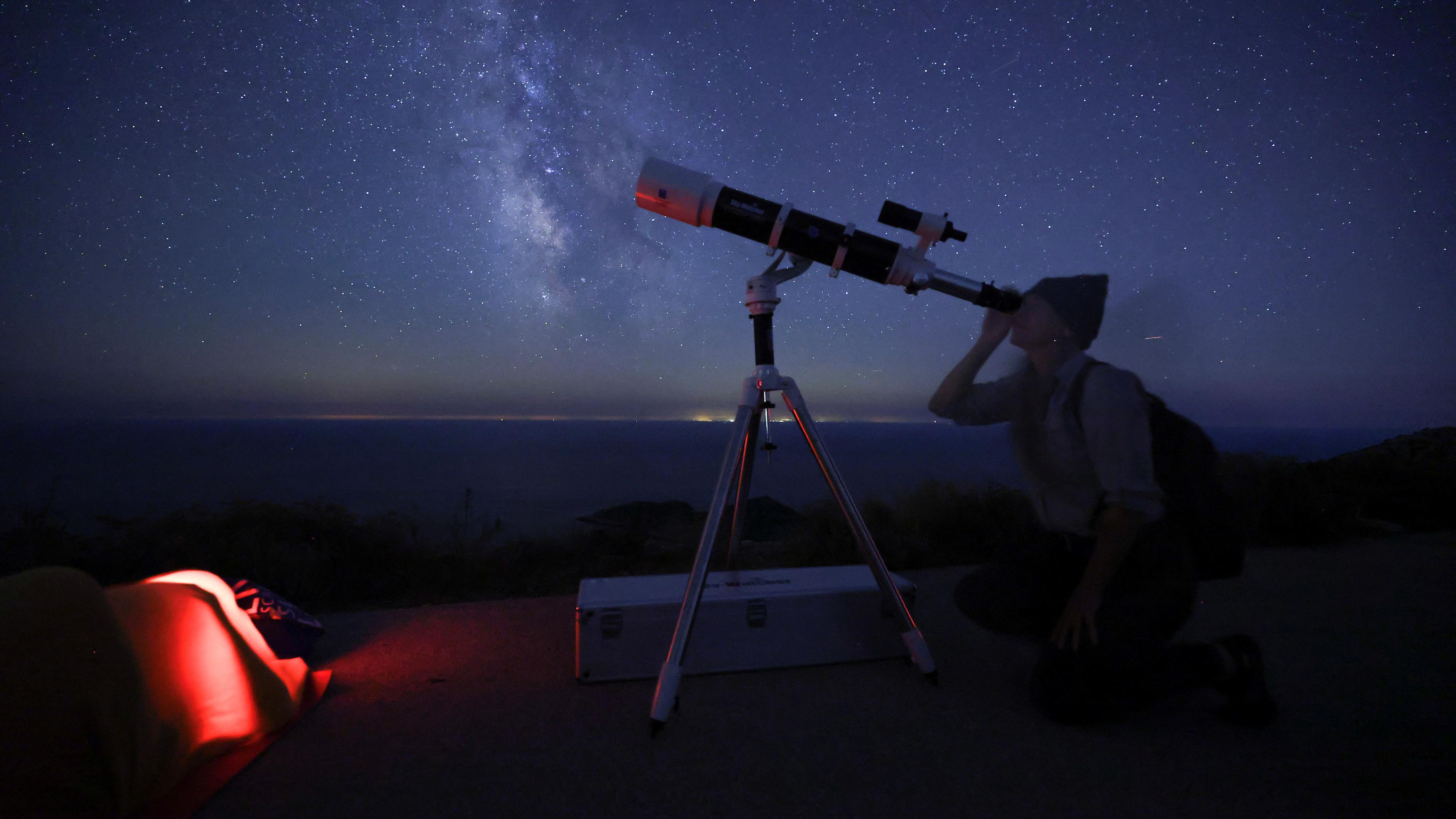 Ein Frau schaut durch ein Teleskop in den Sternenhimmel. 