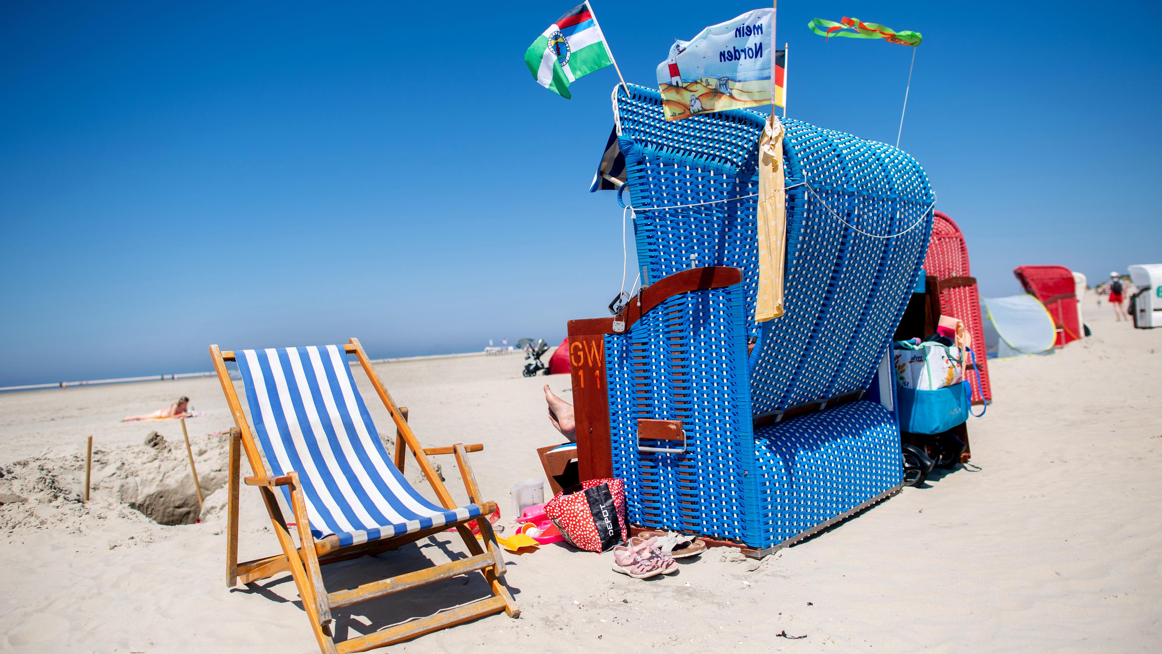 Ein blauer Strandkorb steht neben einem gestreiften Liegestuhl am Strand auf Borkum.