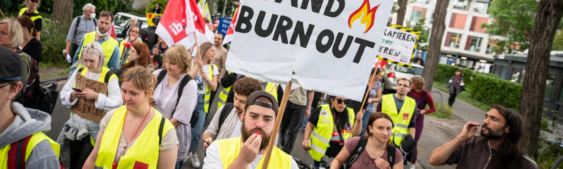 01.06.2022, Nordrhein-Westfalen, Köln: Mit einem Plakat «Pflege - come in and burn out» nehmen Pflegekräfte an einer Demonstration teil. Die Streiks der Beschäftigten an sechs Unikliniken in Nordrhein-Westfalen im Kampf um einen Tarifvertrag Entlastung geht bereits in die siebte Woche. 