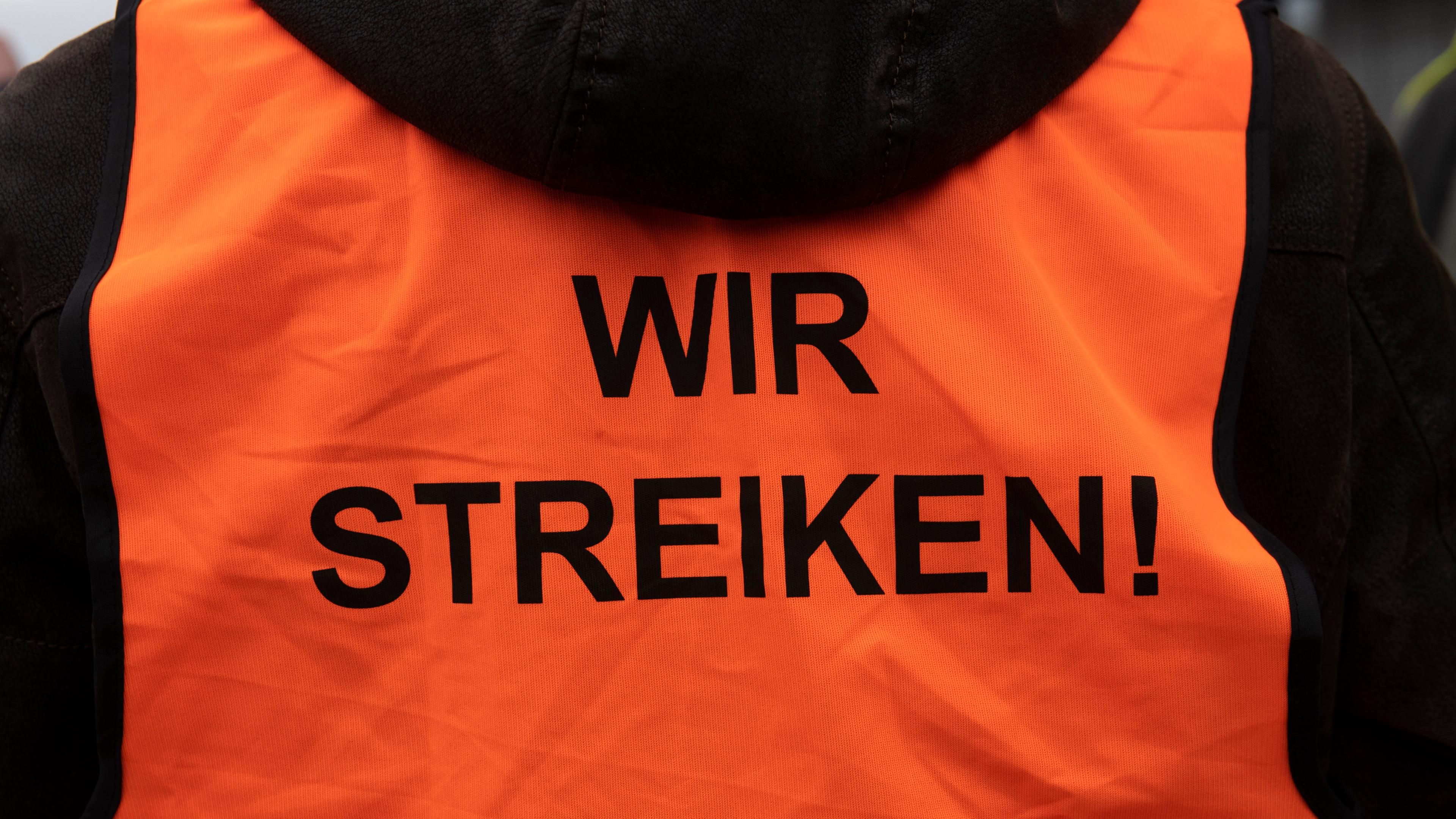 Mensch mit Weste auf dessen Rückseite "wir streiken" geschrieben steht. 