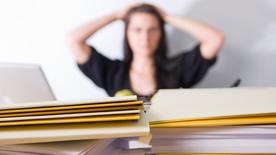 A stressed woman sits in front of Aktenordner (Symbolforo)