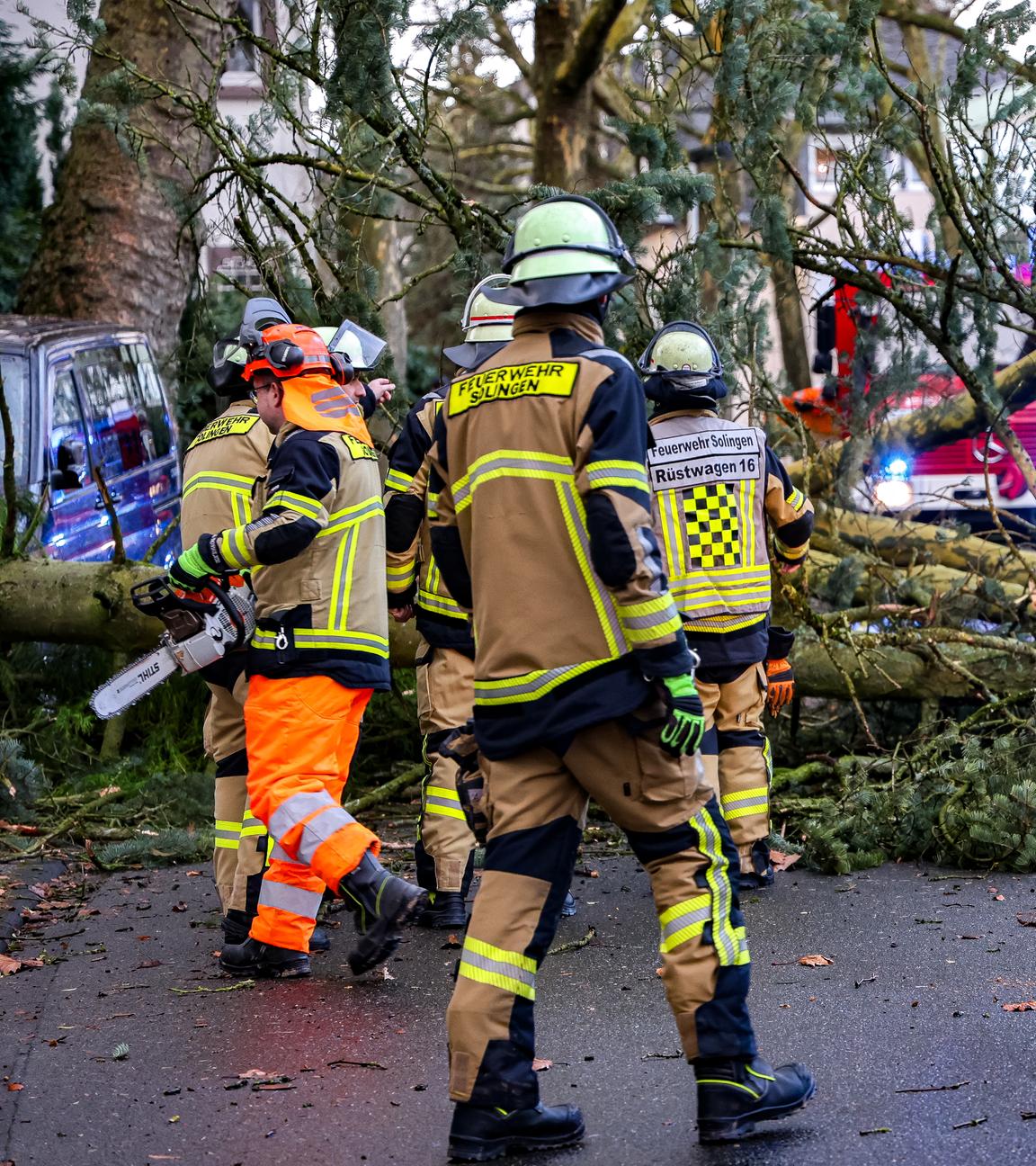 Einsatzkräfte der Feuerwehr zerkleinern einen umgestürzten Baum in Solingen.