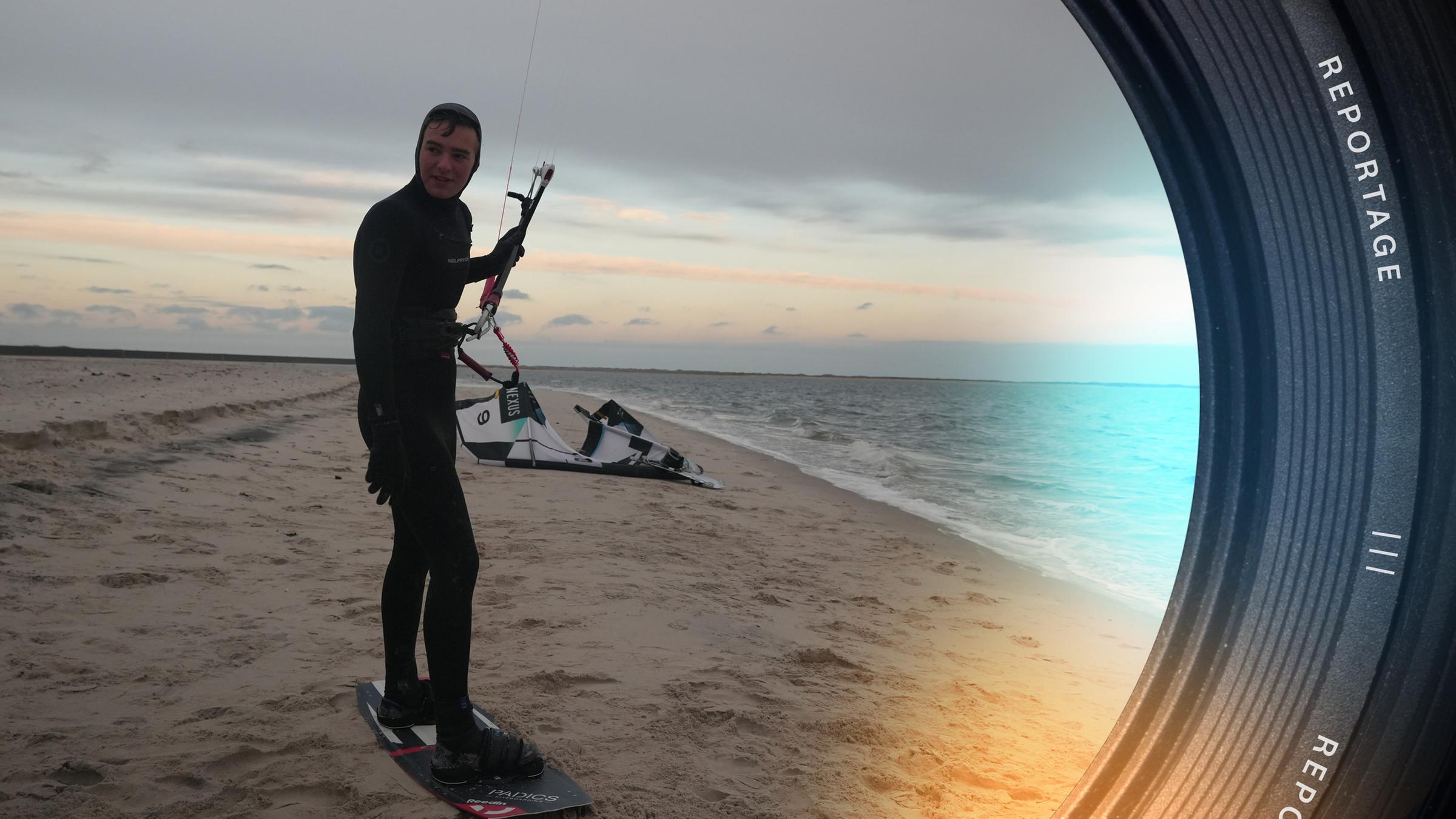 Boy-Ole steht im Neoprenanzug am Strand, in den Händen hält er die Bügel eines Kiteschirms.