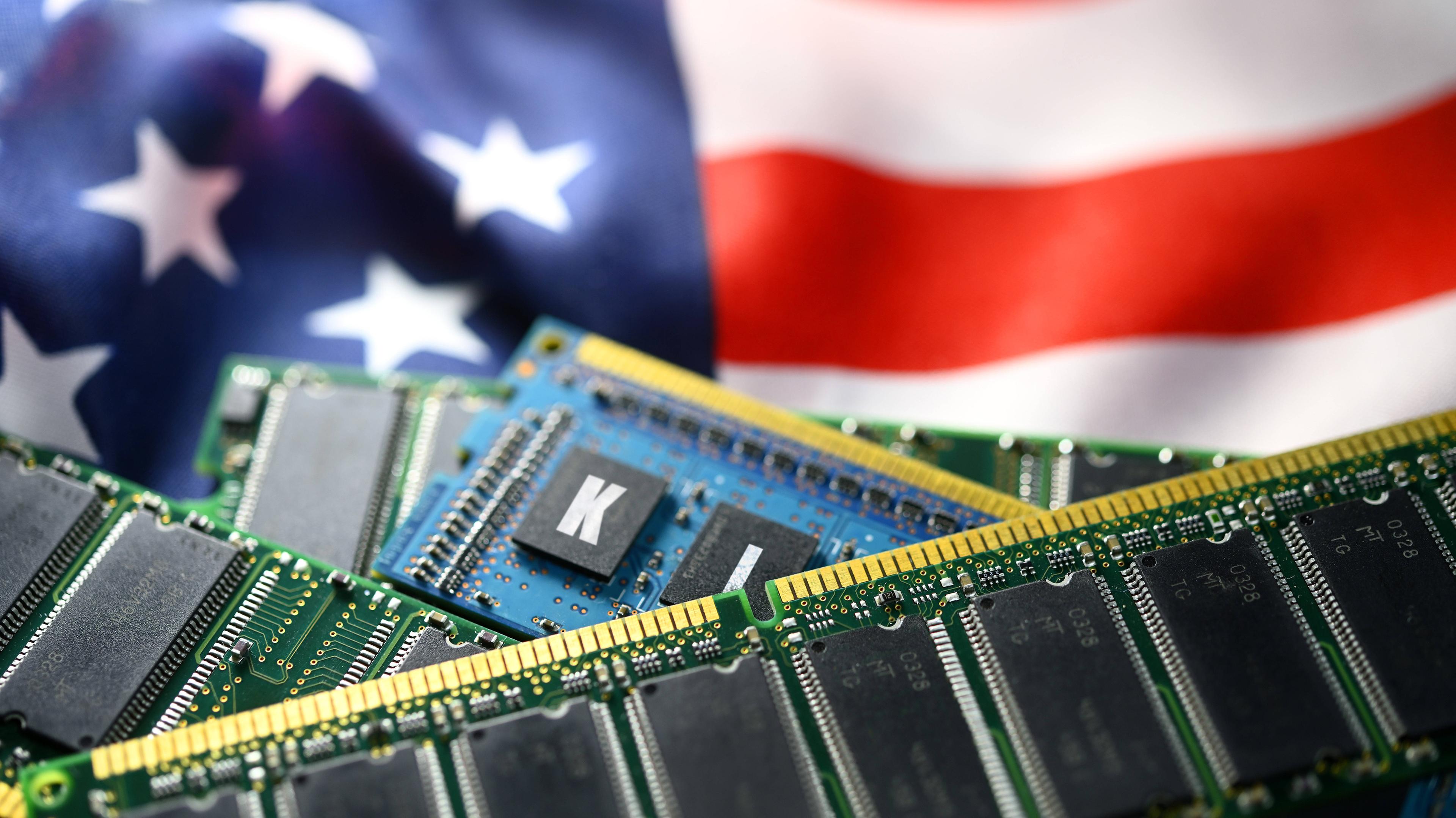 Vor der US-amerikanischen Flagge mit roten streifen und weißen Sternen auf blauem Grund liegen Computer-Chips. Einer trägt die Aufschrift KI