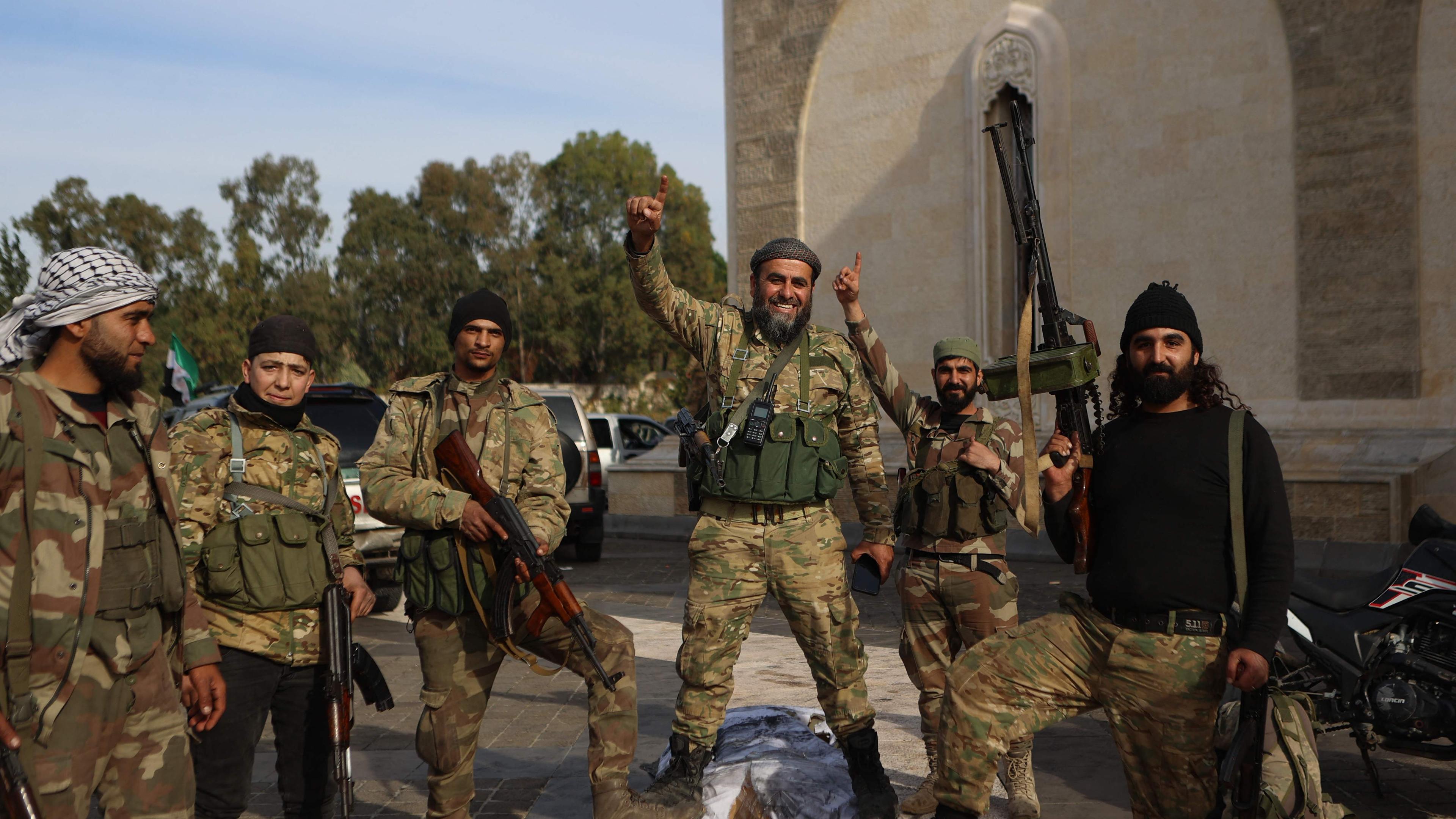 Rebel fighters pose for a picture outside the mausoleum of Syria's late president Hafez al-Assad in the family's ancestral village of Qardaha in the western Latakia province on December 11, 2024, after it was stormed by opposition factions and his gravesite set ablaze