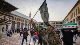 A masked opposition fighter carries a Hayat Tahrir al-Sham (HTS) flag in the courtyard of the Umayyad Mosque in the old walled city of Damascus, Syria, Tuesday, Dec. 10, 2024. HTS is the main rebel faction in opposition that toppled Bashar Assad's regime on Sunday . (AP Photo/Hussein Malla)