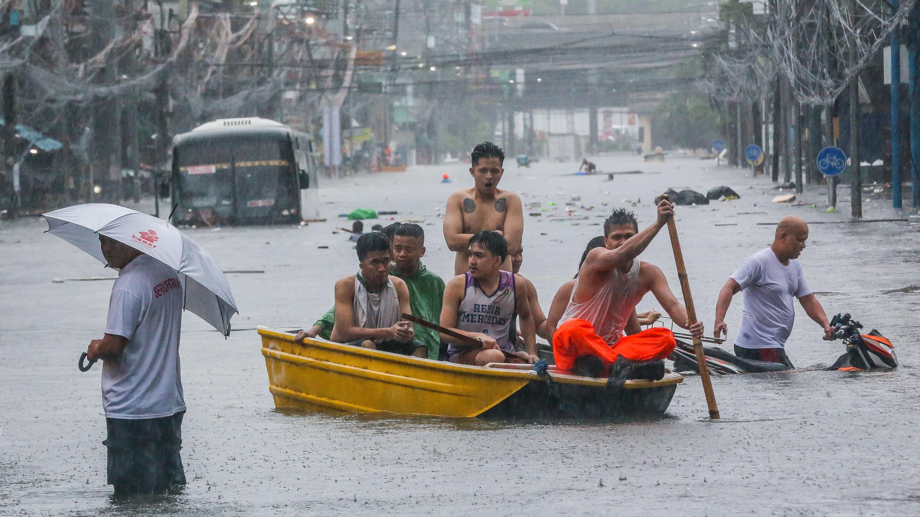 24.07.2024, Philippinen, Quezon City: Einwohner rudern mit einem Boot auf einer überfluteten Straße in Quezon City.