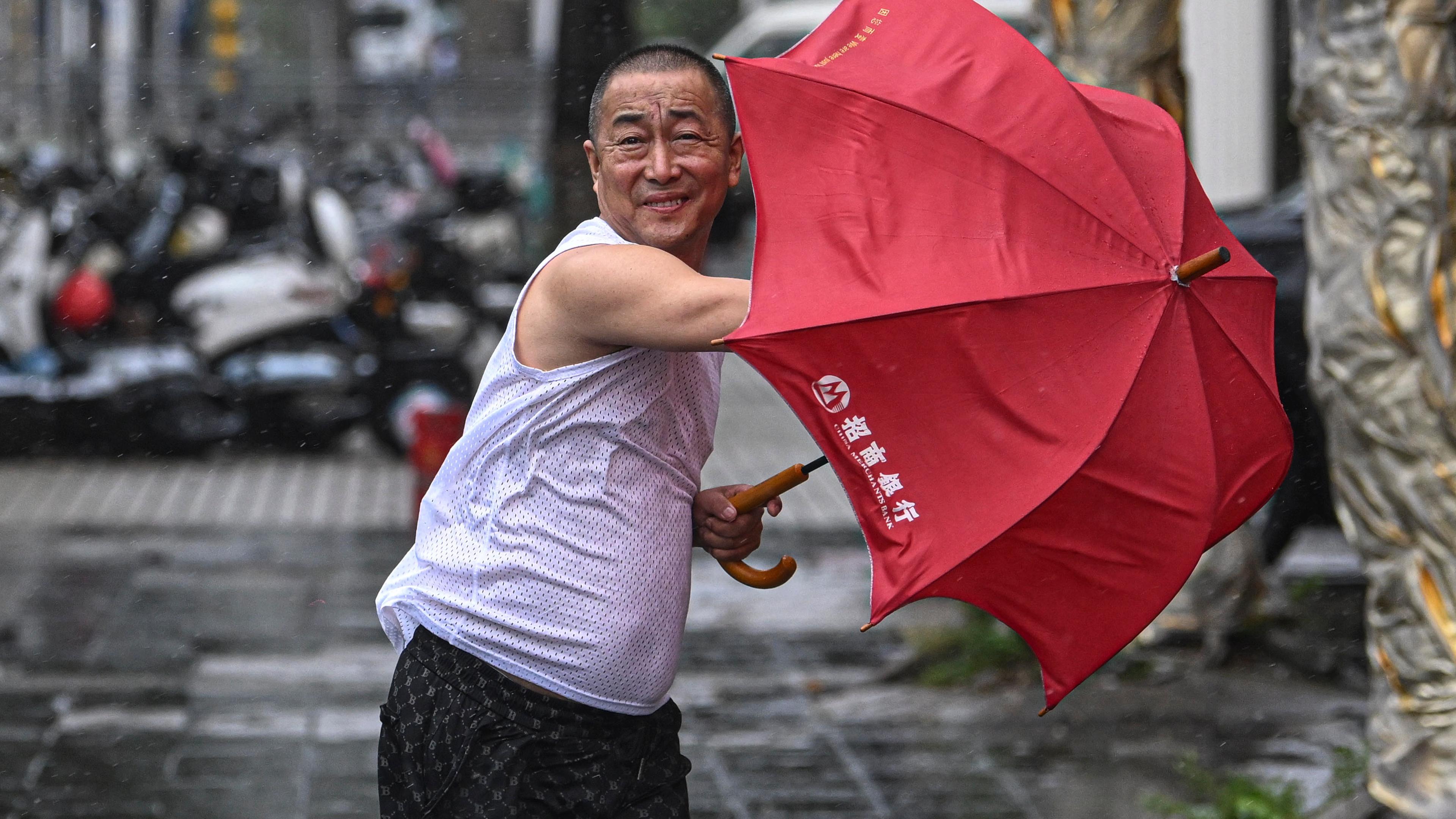 Ein Mann hält einen roten Regenschrim im Sturm