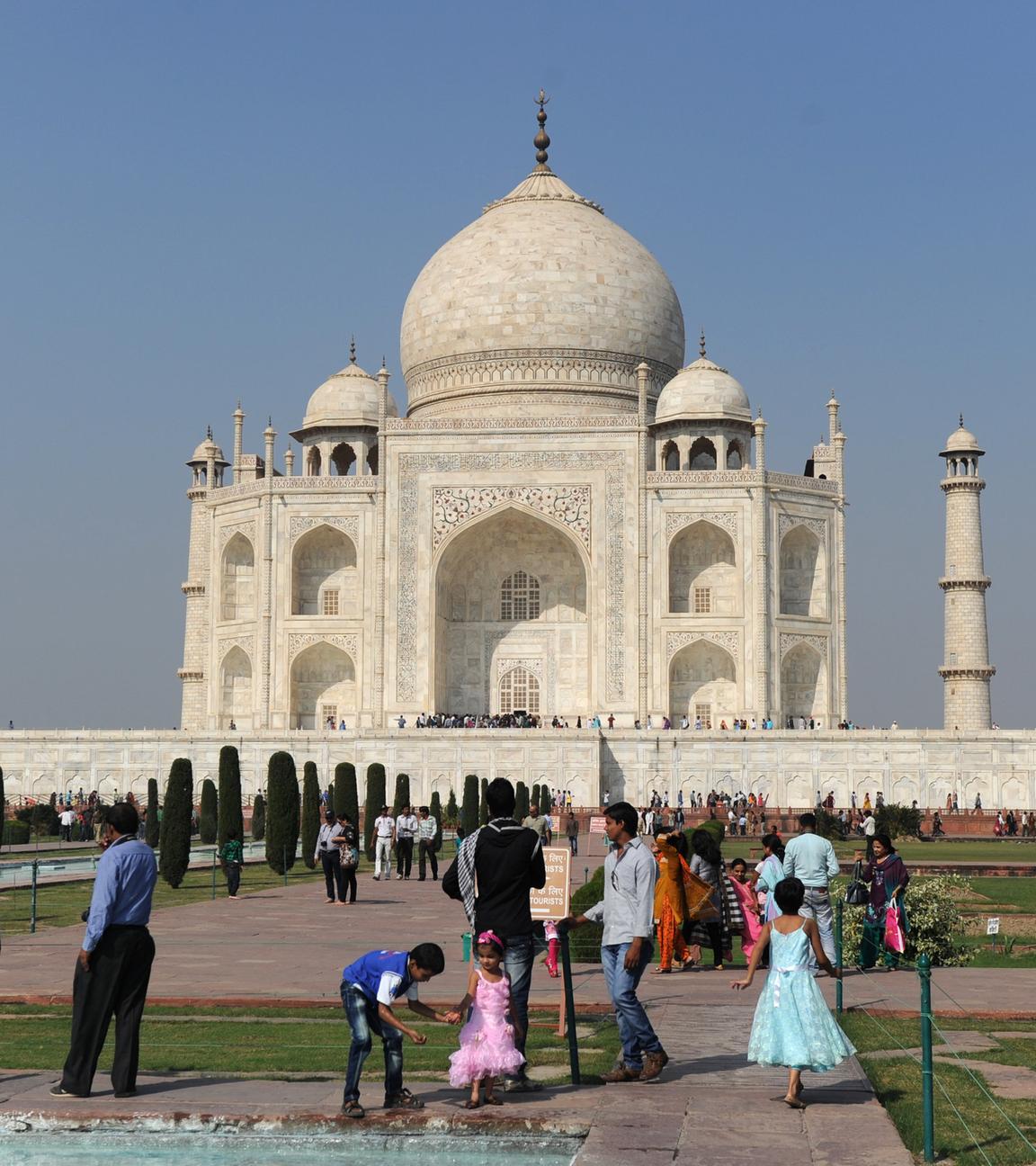 Das Taj Mahal steht vor wolkenfreiem Himmel. Menschen befinden sich auf dem Gelände.