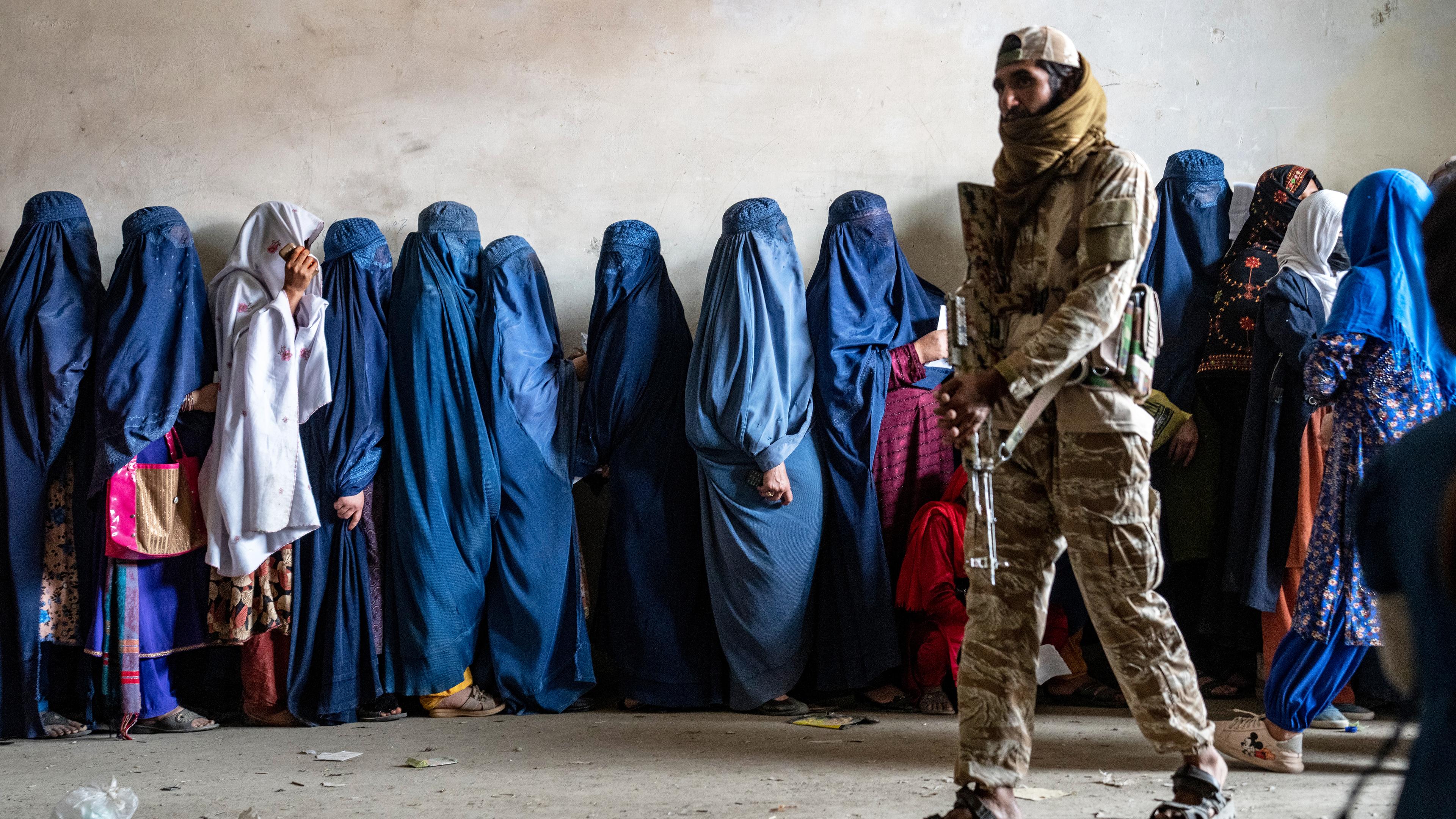 Ein Taliban-Kämpfer steht Wache, während Frauen in Kabul darauf warten, Lebensmittelrationen zu erhalten