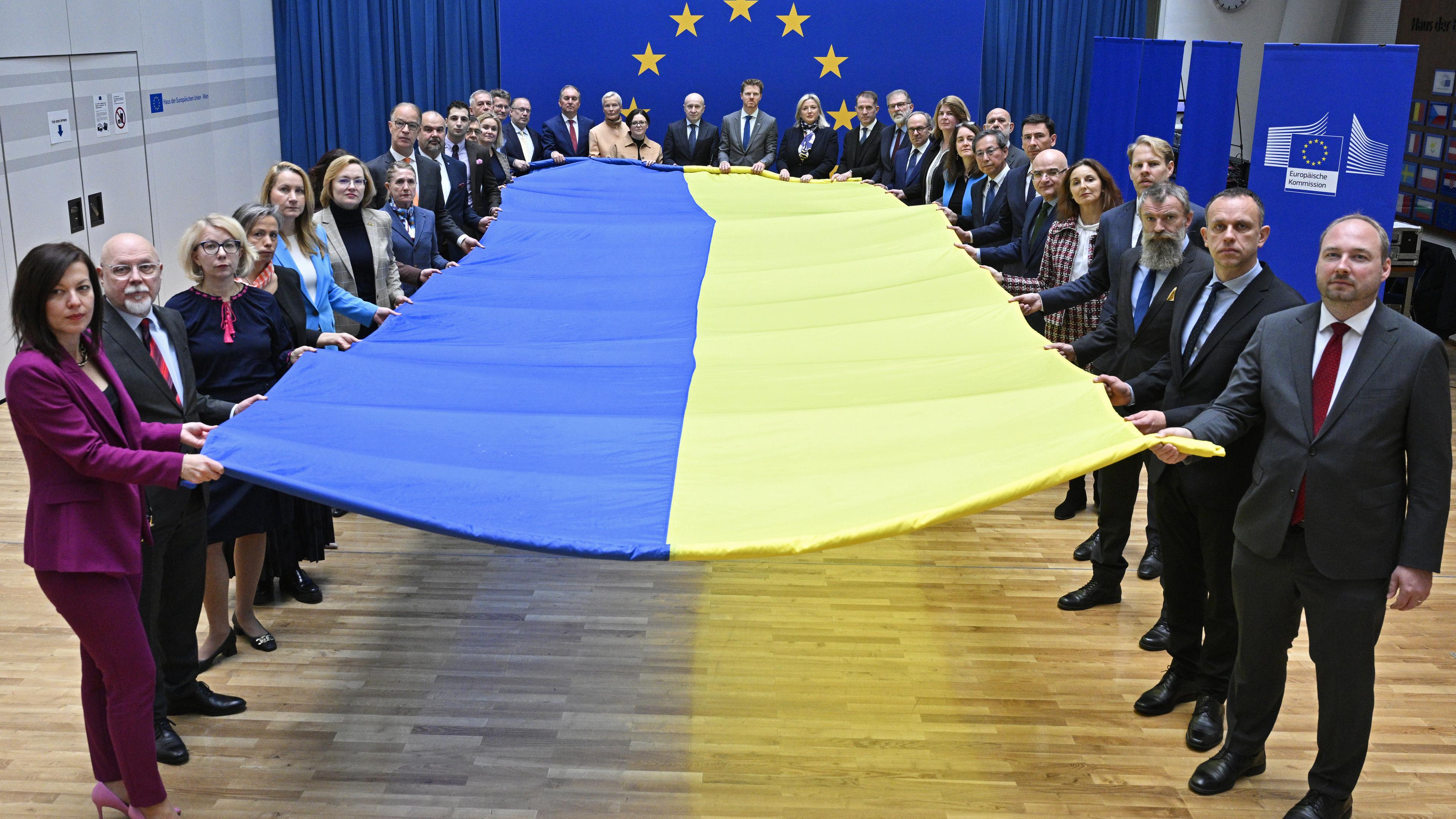 Botschafterinnen und Botschafter der EU-Staaten, der EU-Beitrittskandidaten und der G7 halten eine große Fahne beim Fototermin «1000 Tage Krieg - Solidarität mit der Ukraine» im Haus der Europäischen Union. 