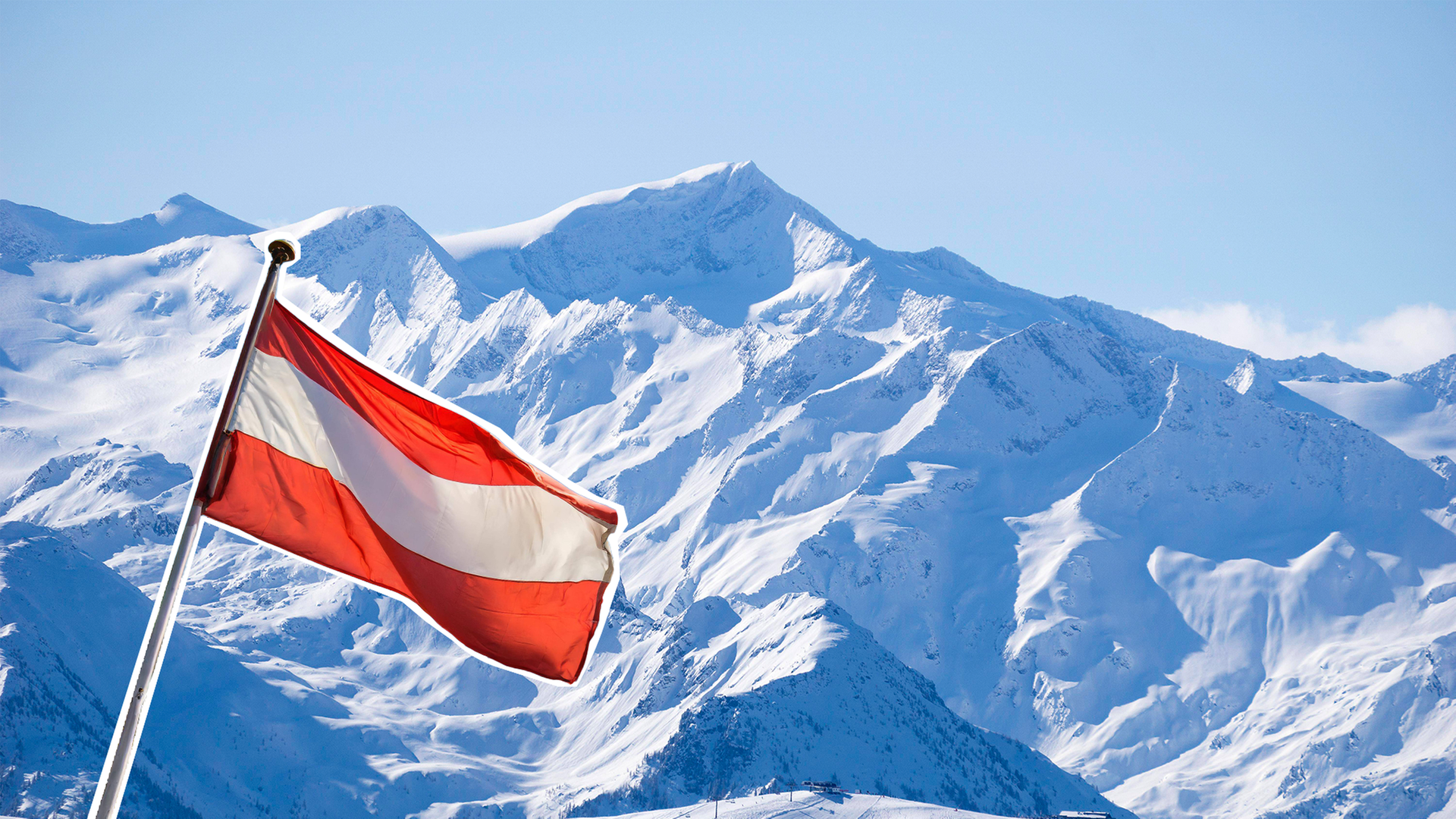 eine Berglandschaft mit viel Schnee. Davor weht eine österreichische Flagge im Wind.