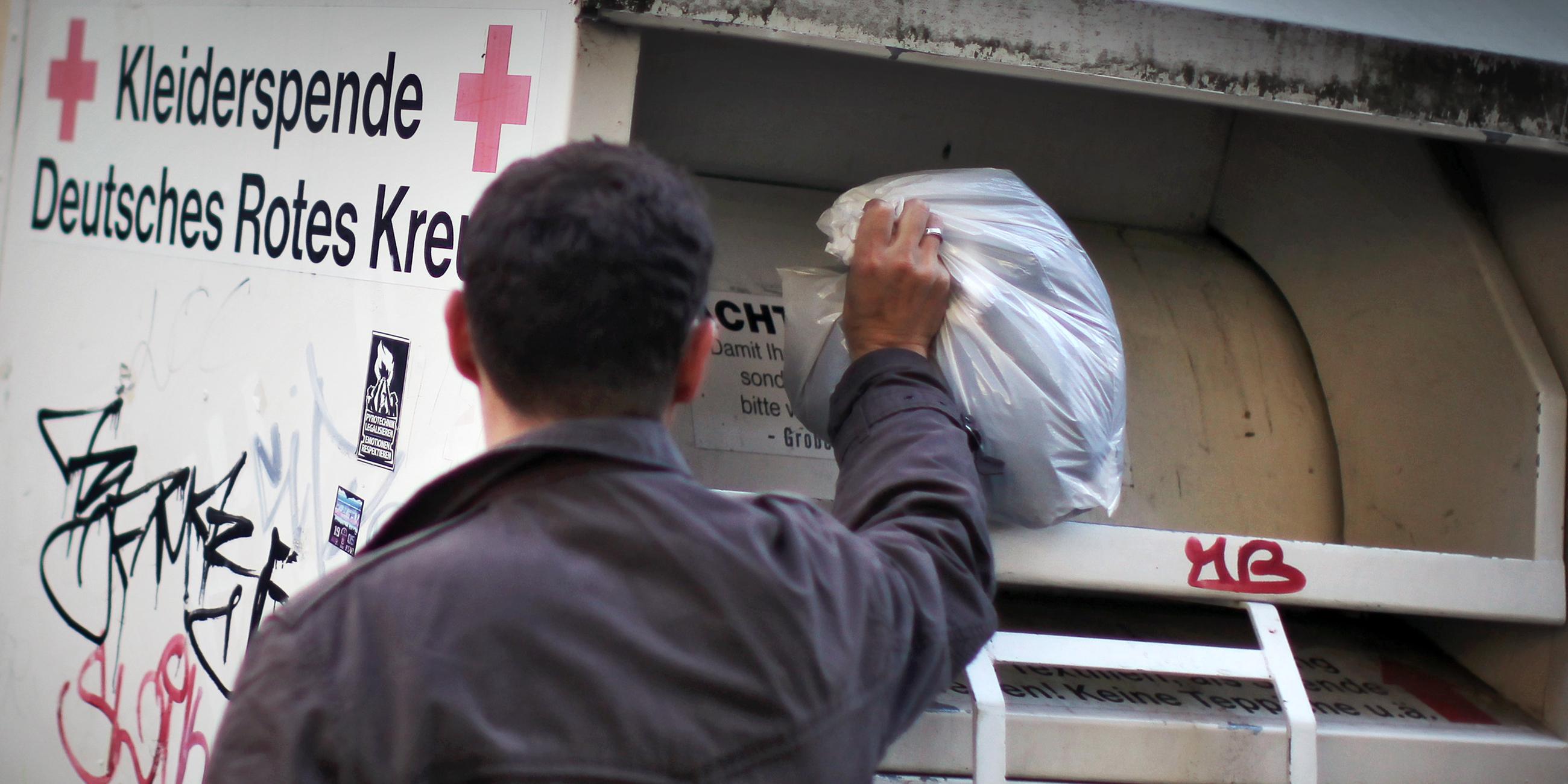 Mann wirft Kleidung in Altkleidercontainer