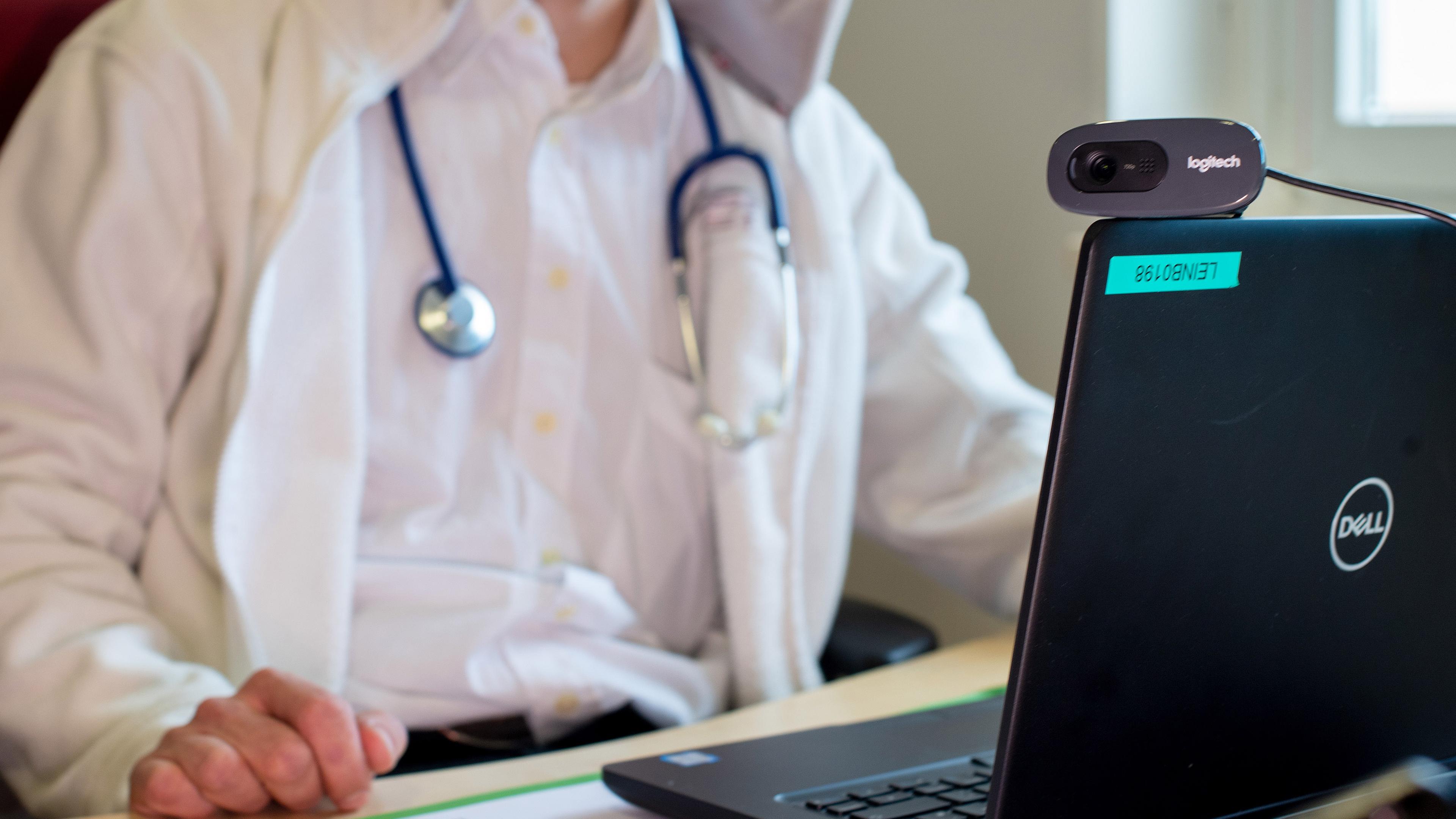 Ein Arzt sitzt vor einem Laptop und hält eine Videosprechstunde.