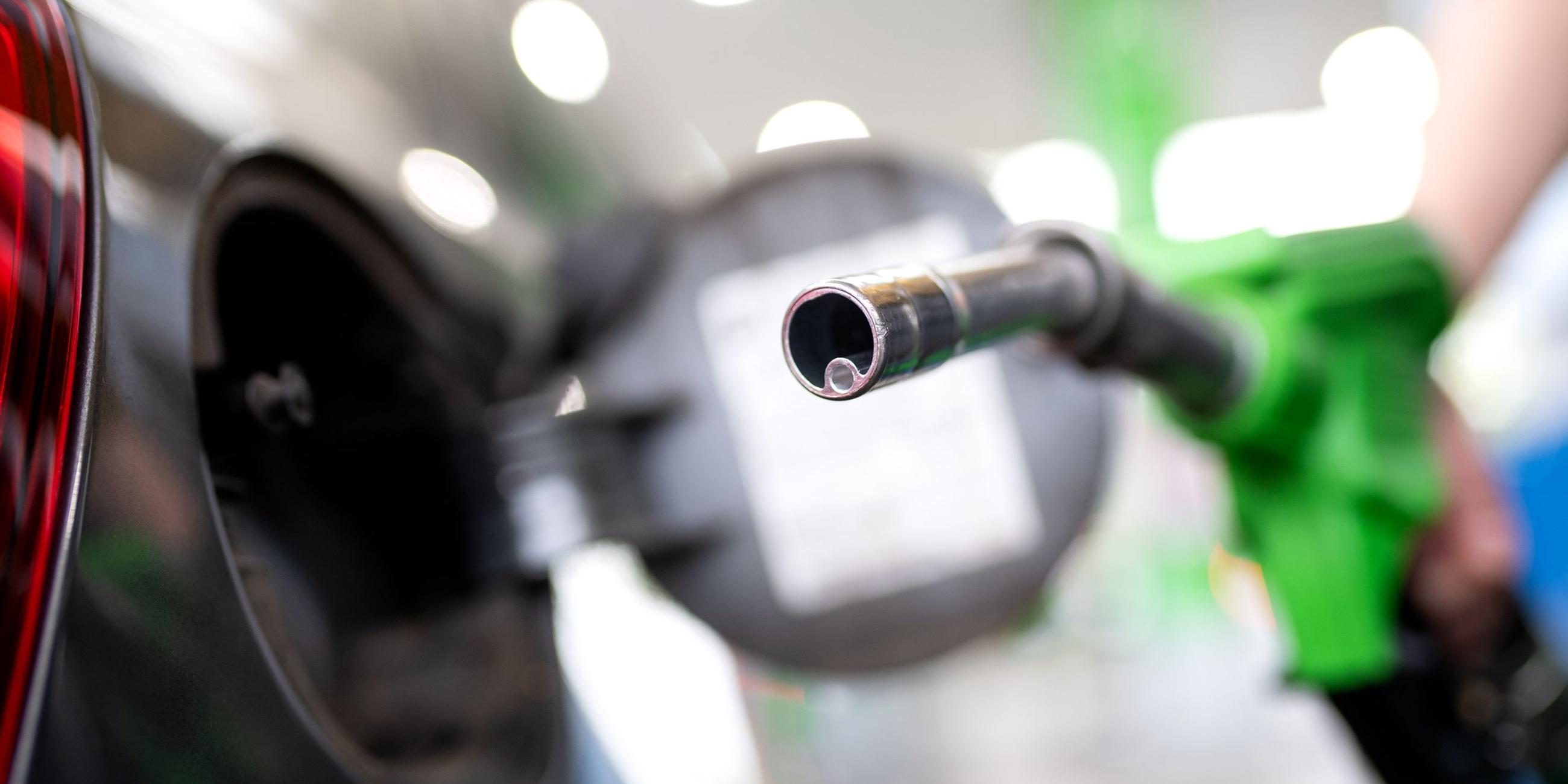 Frau hält an einer Tankstelle eine Zapfpistole. Symbolpolitik