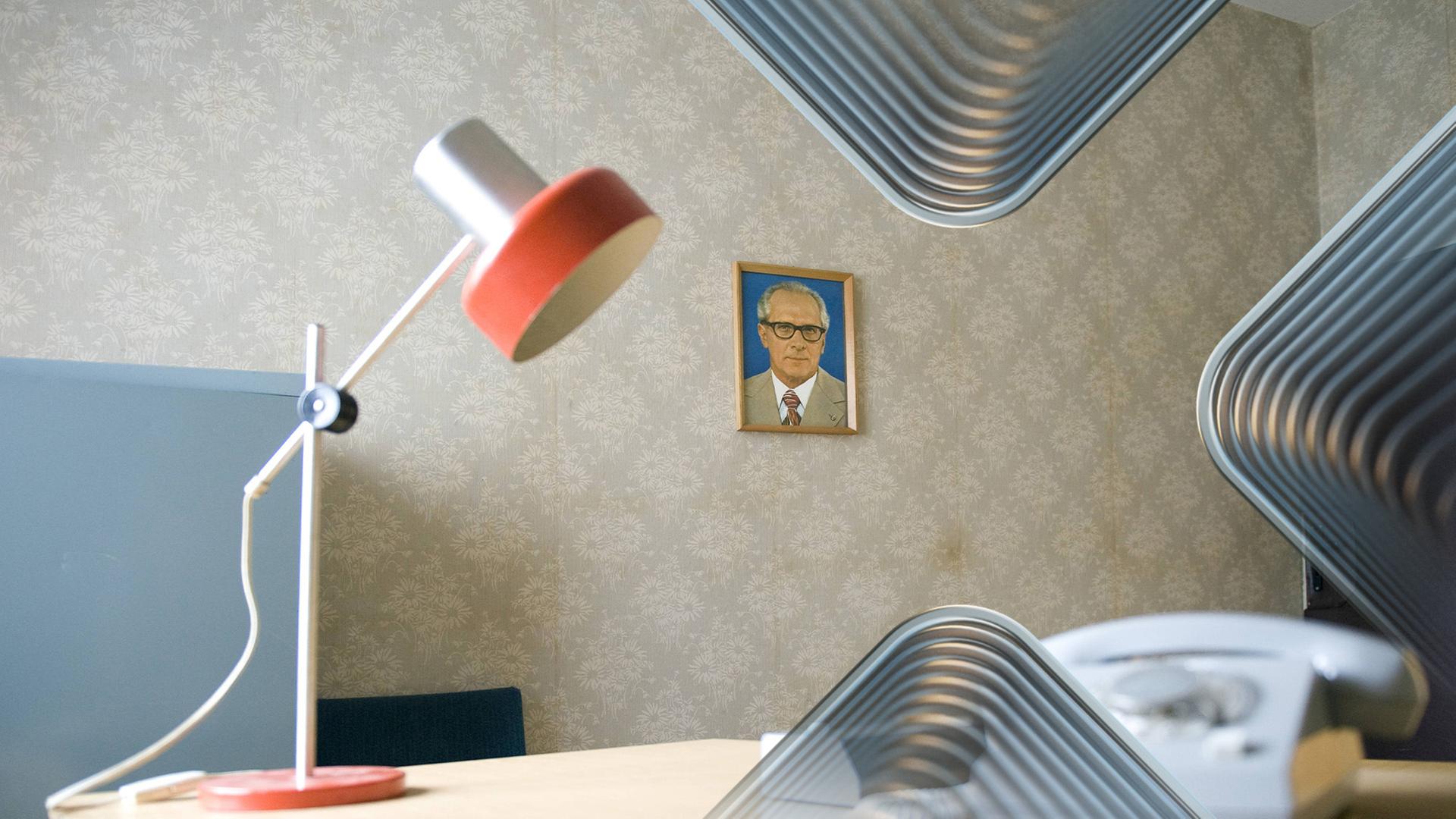 Büro der Staatssicherheit mit Retro-Schreibtischlampe, Wählscheibentelefon und Bild von Erich Honecker an der Wand