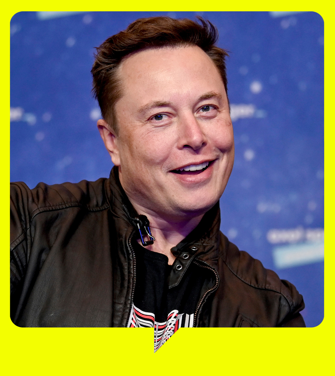 Elon Musk steht vor einer blauen Wand und zeigt zwei Daumen hoch in die Kamera.