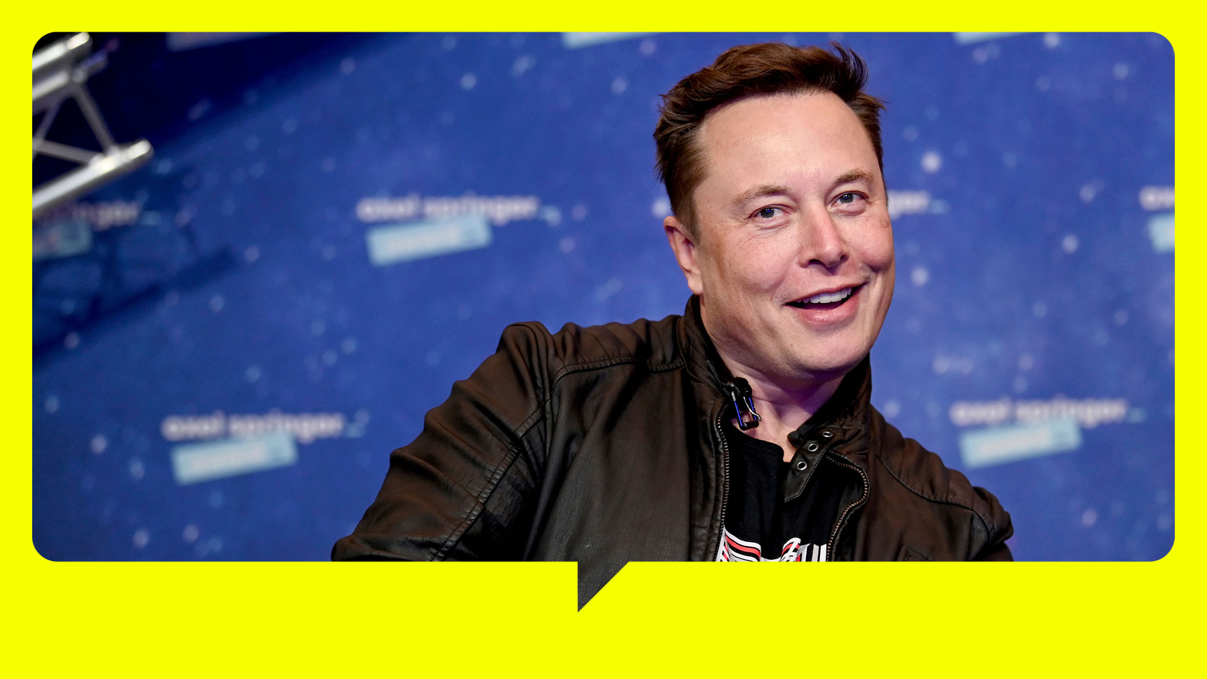 Elon Musk steht vor einer blauen Wand und zeigt zwei Daumen hoch in die Kamera.