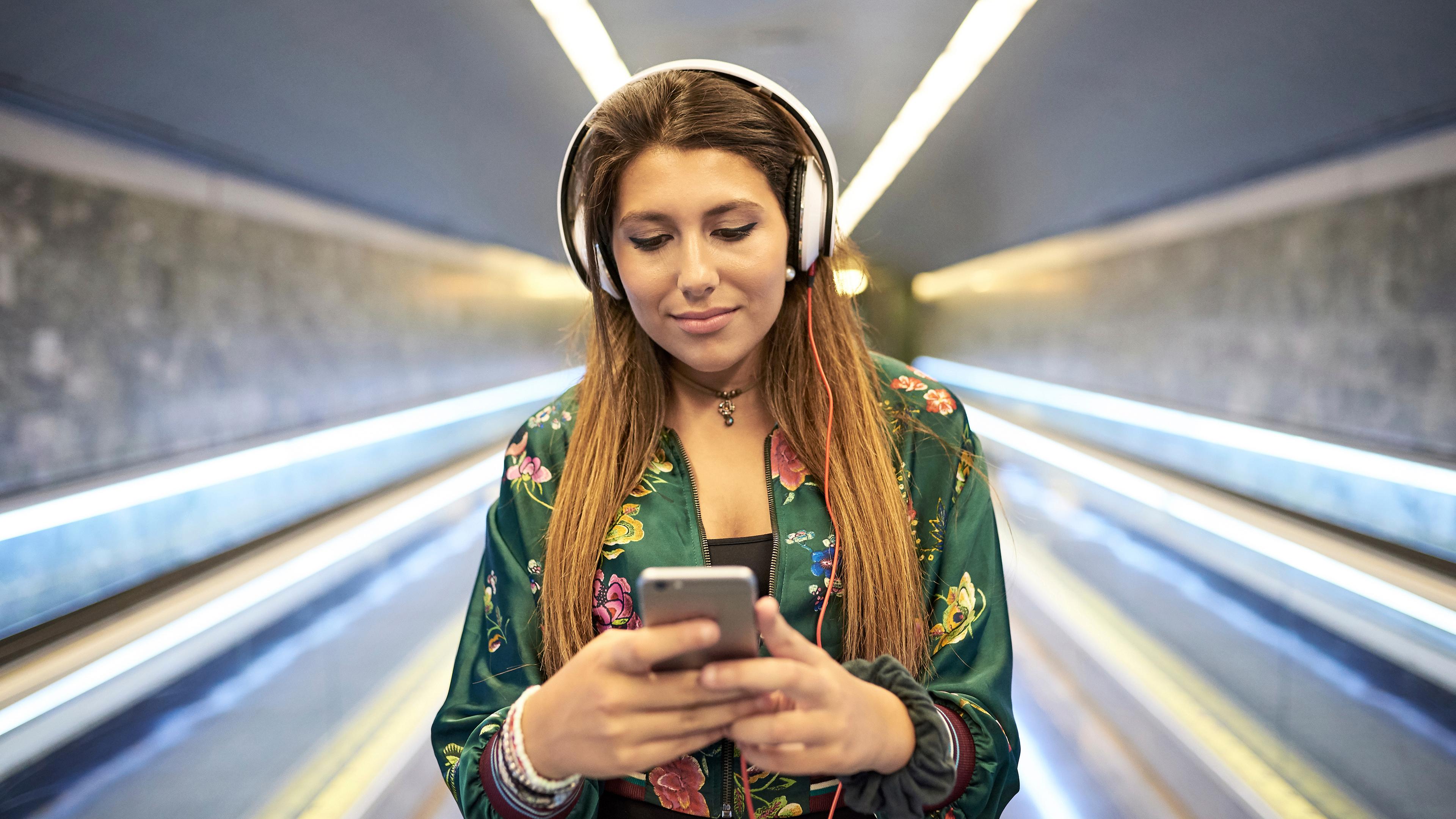 Eine junge Frau mit Kopfhörern streamt Musik über ihr Smartphone.