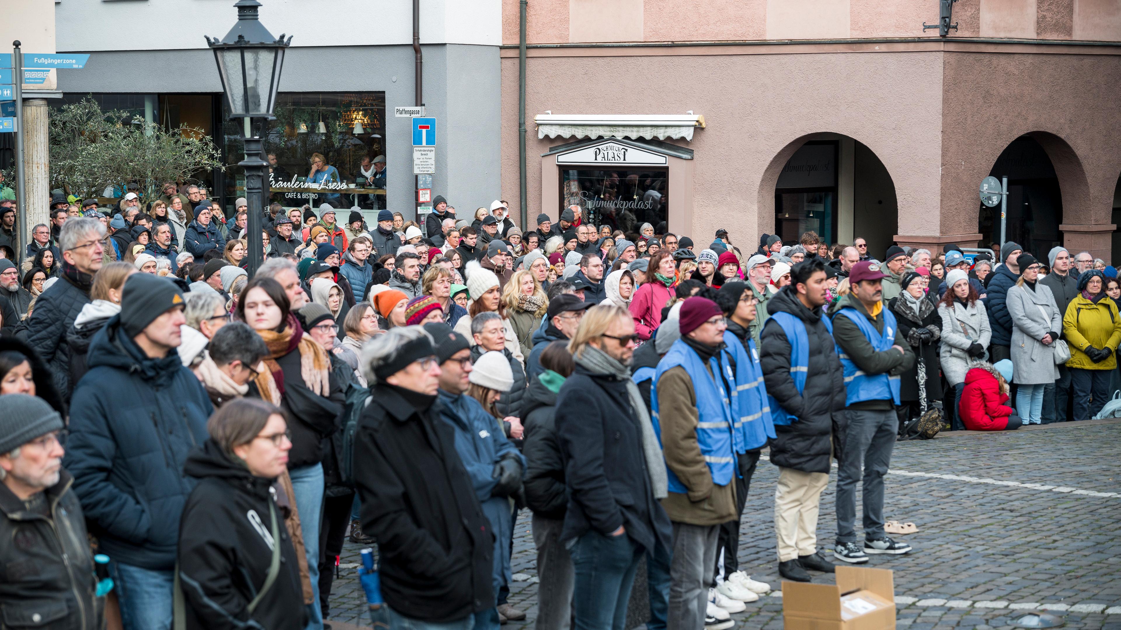  Zahlreiche Menschen haben sich auf dem Platz vor der Stiftsbasilika St. Peter und Alexander versammelt, um am Gottesdienst, der auf einer Leinwand übertragen wird, teilzunehmen.