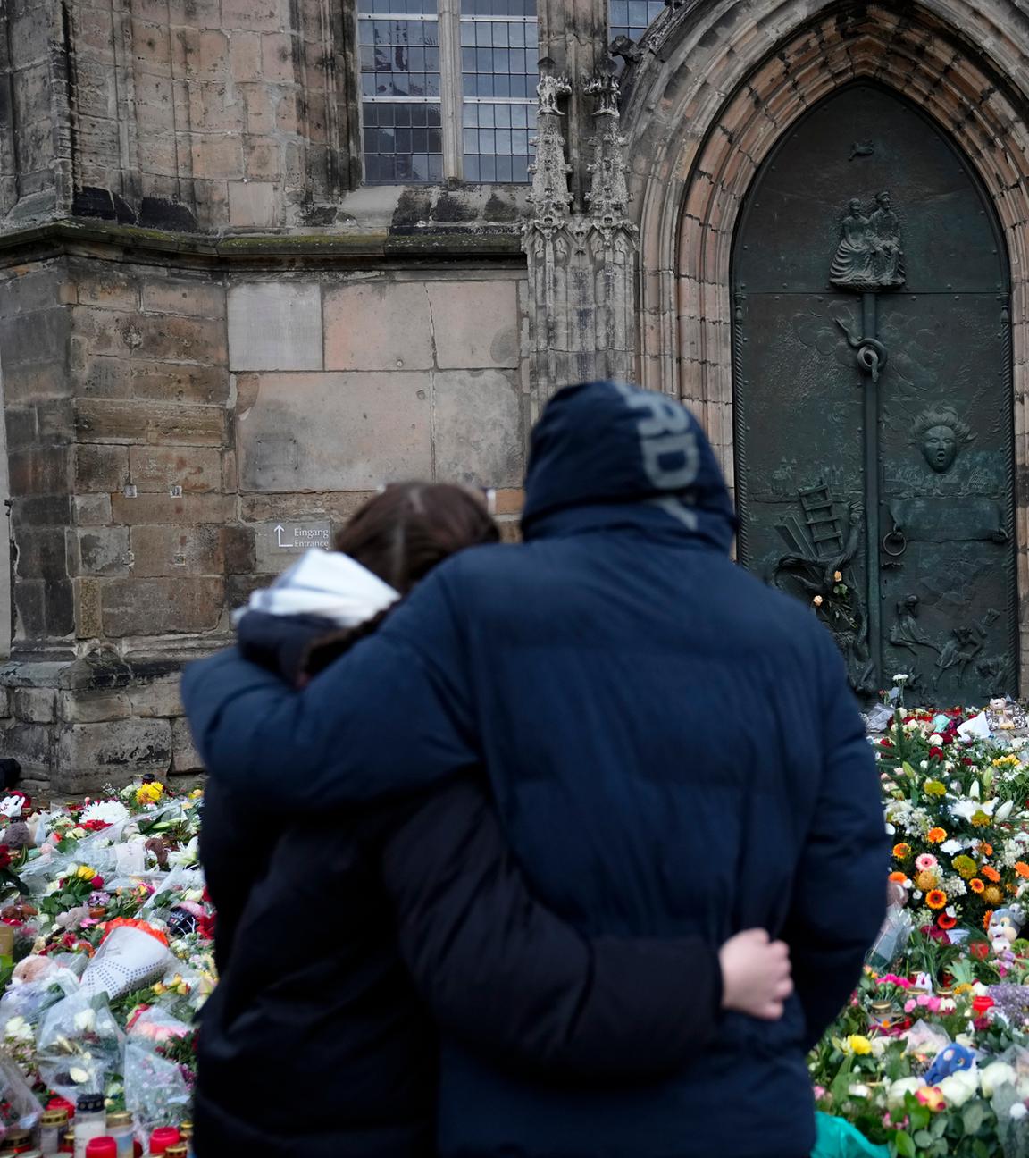 Ein Paar steht Arm in Arm vor Blumen und Kerzen vor der Johanniskirche in Magdeburg.