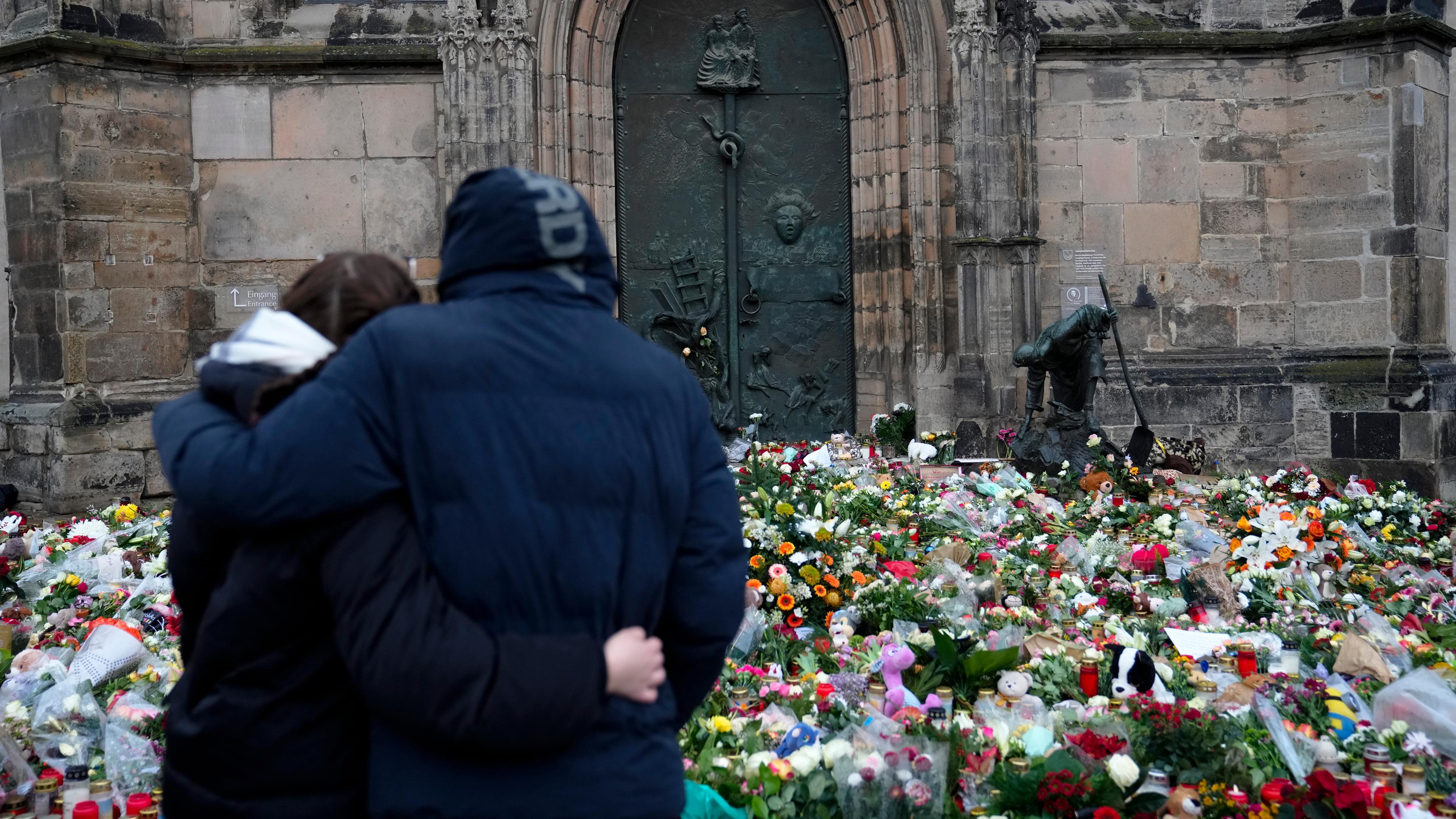 Ein Paar steht Arm in Arm vor Blumen und Kerzen vor der Johanniskirche in Magdeburg.