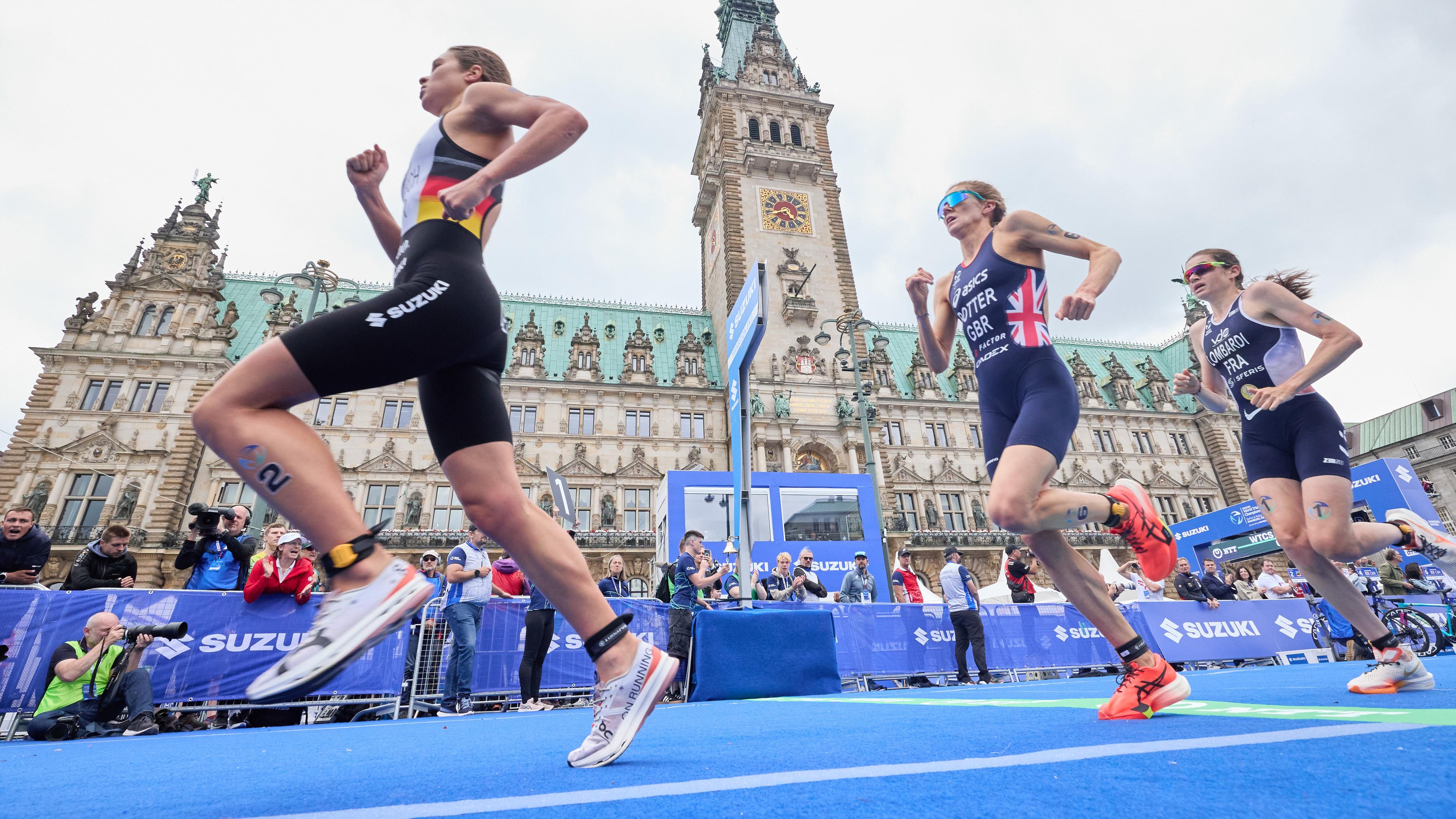 Die Teilnehmerinnen des Triathlon laufen am Hamburger Rathaus vorbei.