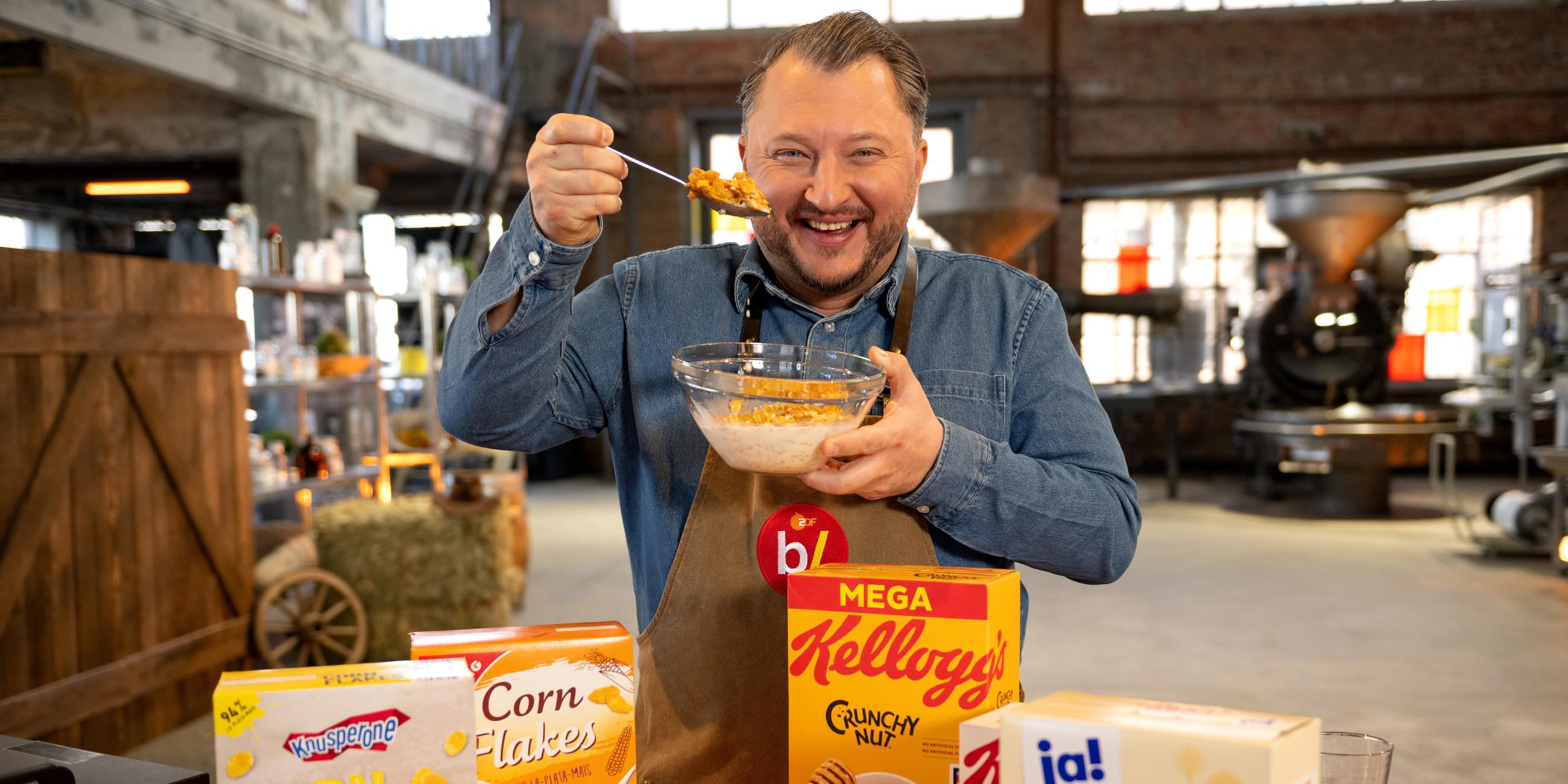 Sebastian Lege steht vor unterschiedlichen Packungen mit Cornflakes und lässt Flakes in eine Schüssel rieseln.