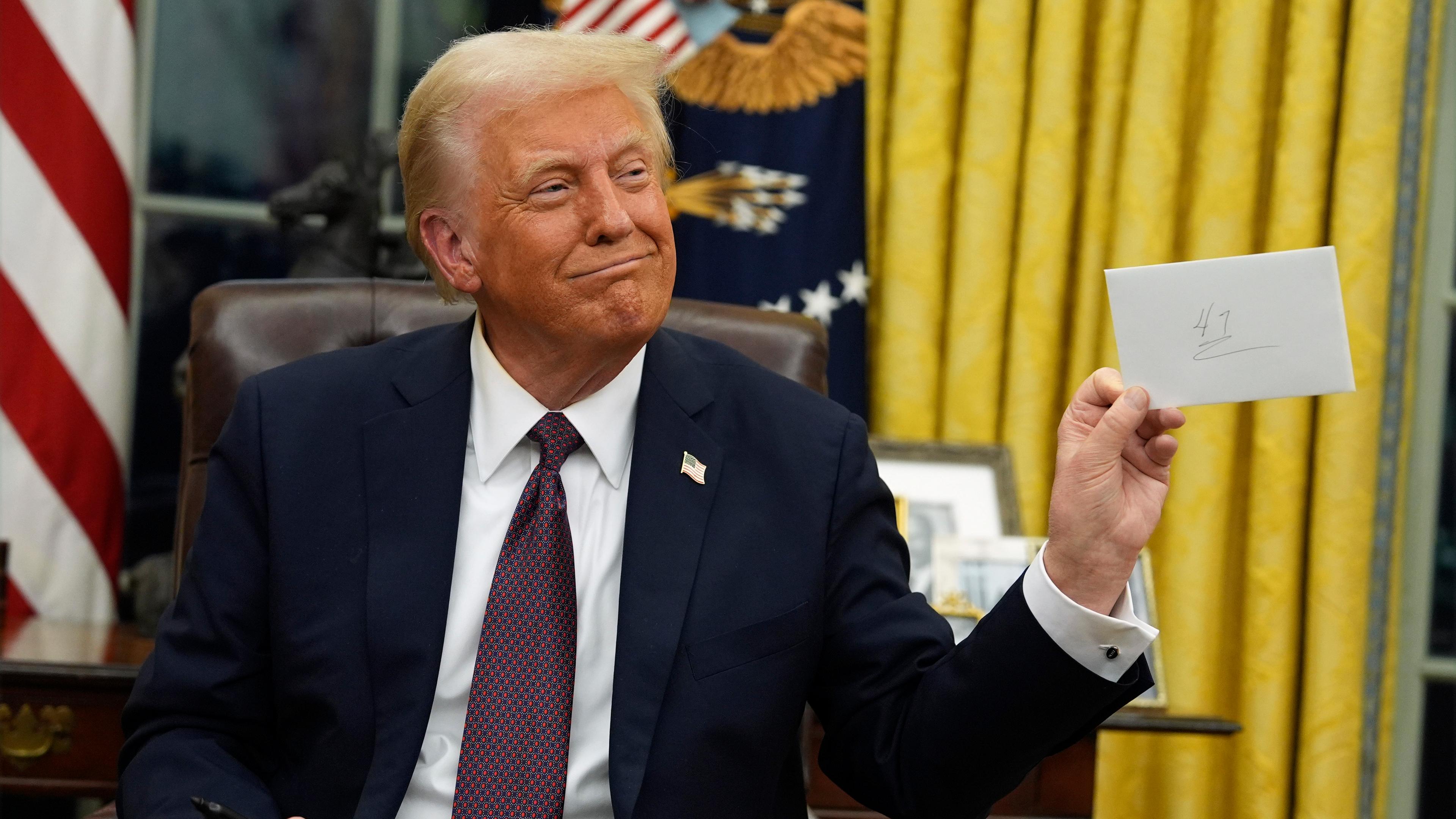 President Donald Trump holds up the letter that former President Joe Biden left for him in the desk as he signs executive orders in the Oval Office of the White House