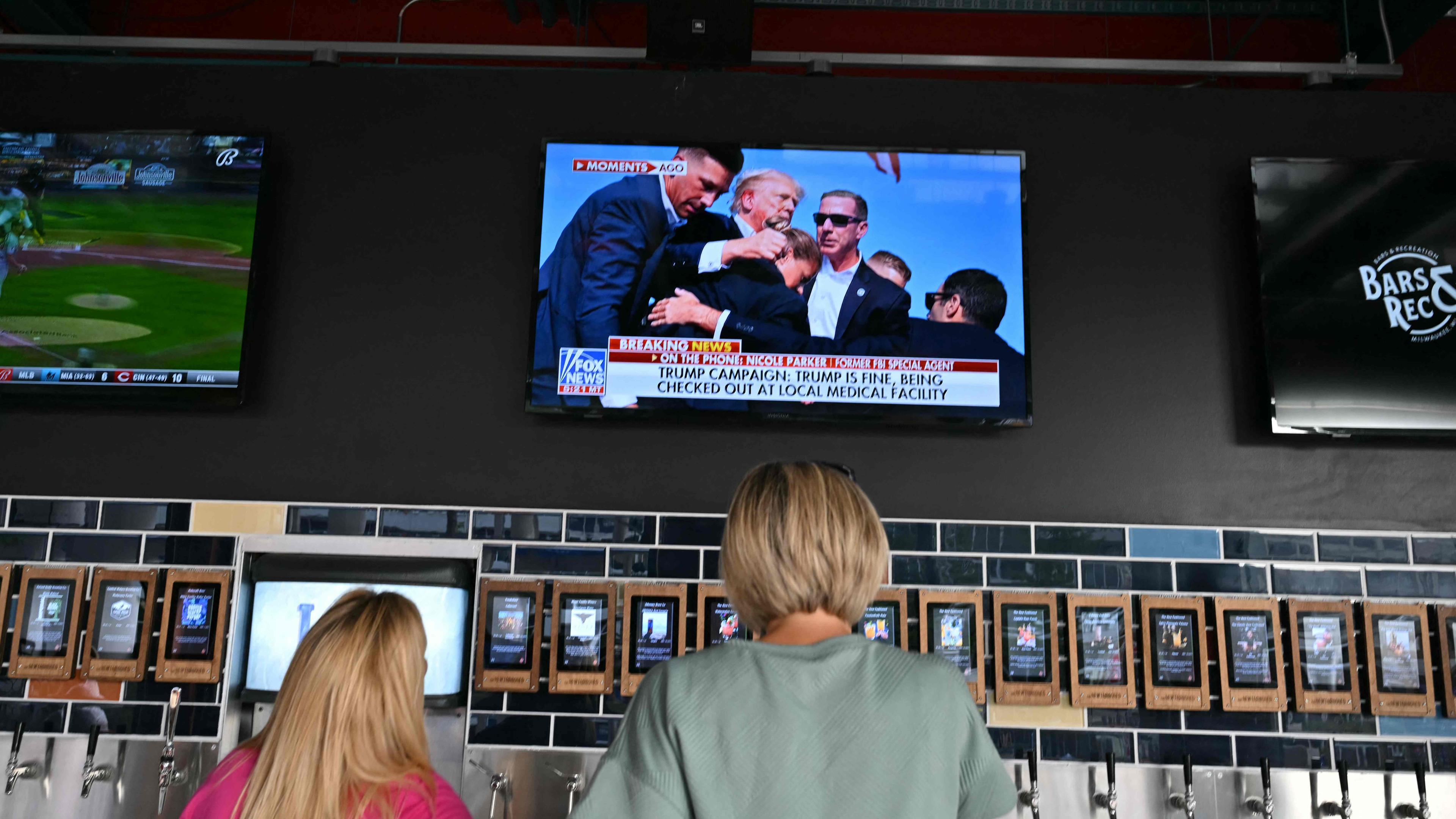 Menschen schauen die Nachrichten zum Trump-Attentat vor einem Fernseher.