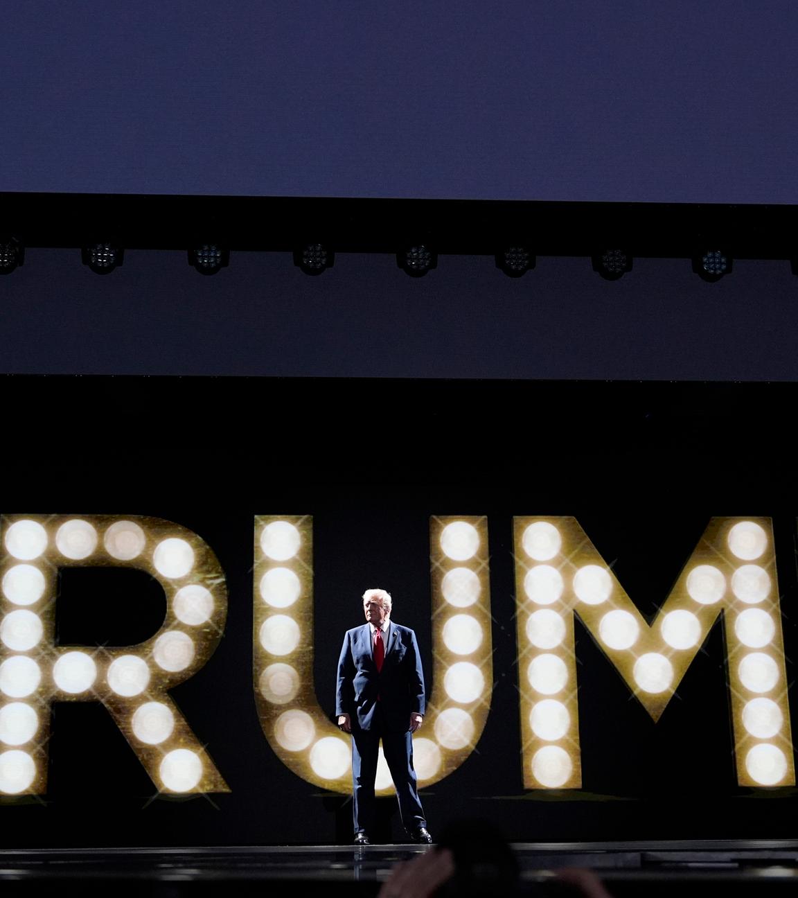 In riesigen Leuchtbuchstaben ist Trump zu lesen, davor steht im Anzug Donald Trump 