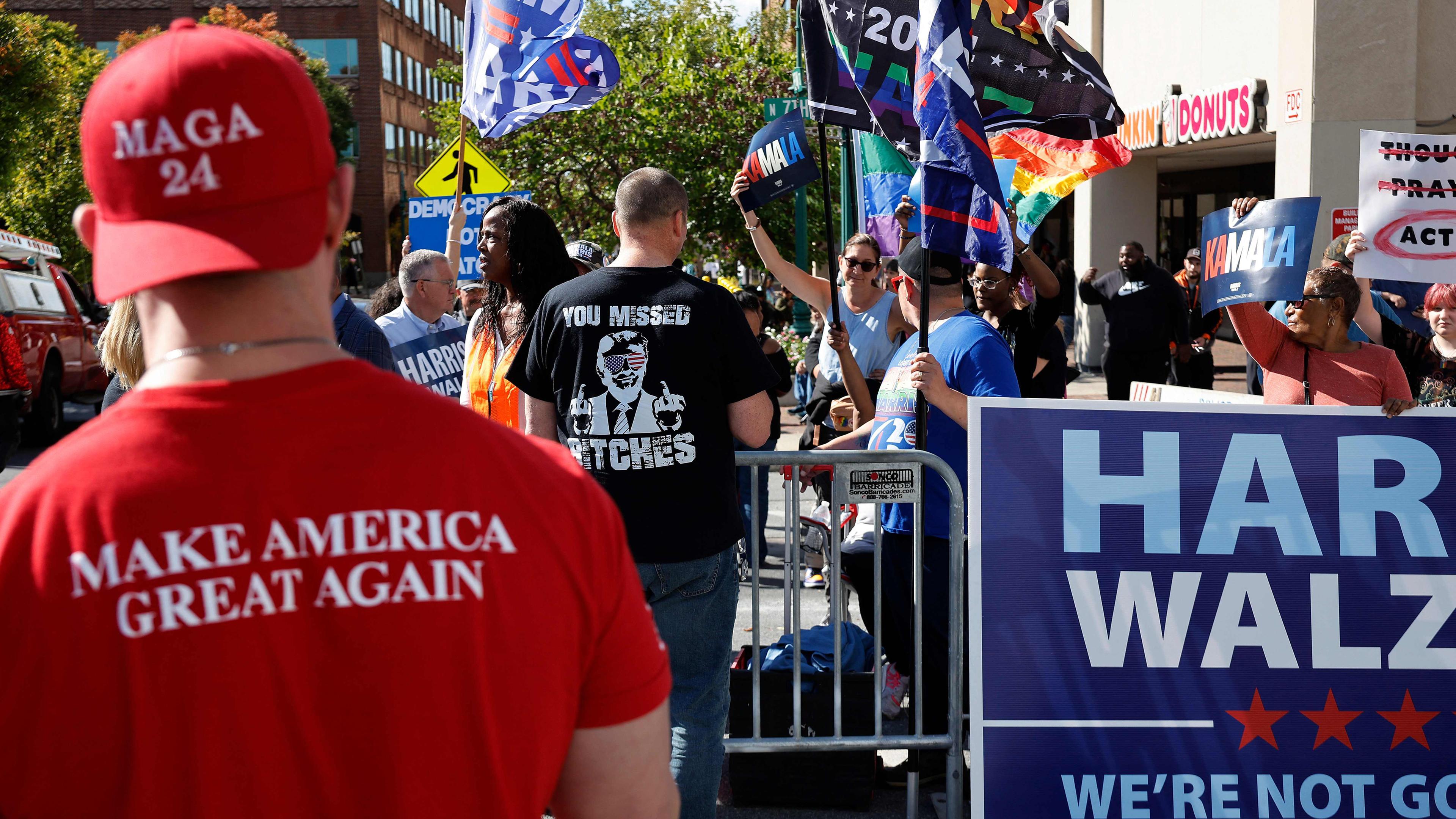 Auf dem Bild sind Unterstützer von Kamala Harris und eine Person, die ein rotes "Make America great again"-Shirt trägt.