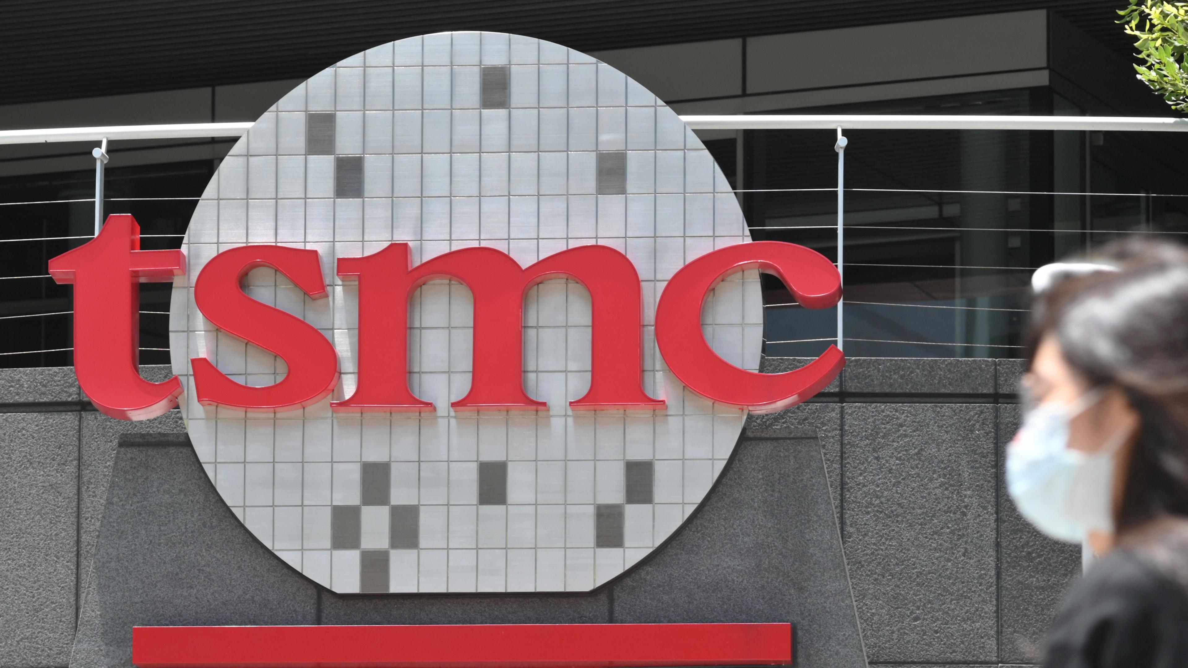 Das Logo der TSMC, am Rand läuft eine Frau mit Maske ins Bild