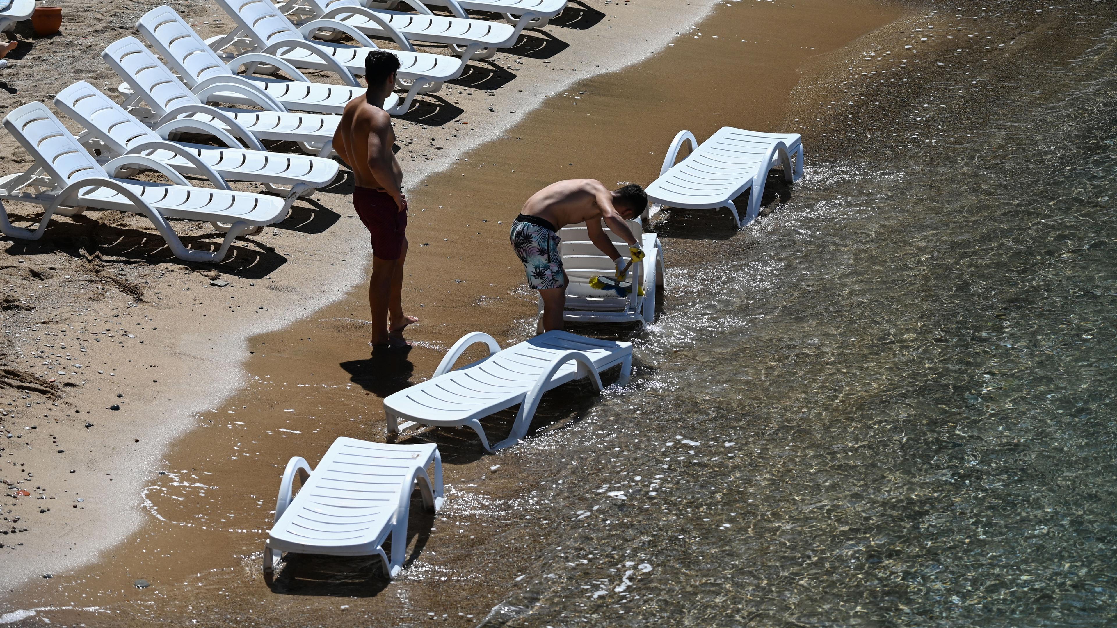 Ein Mann reinigt im Meer Liegestühle.