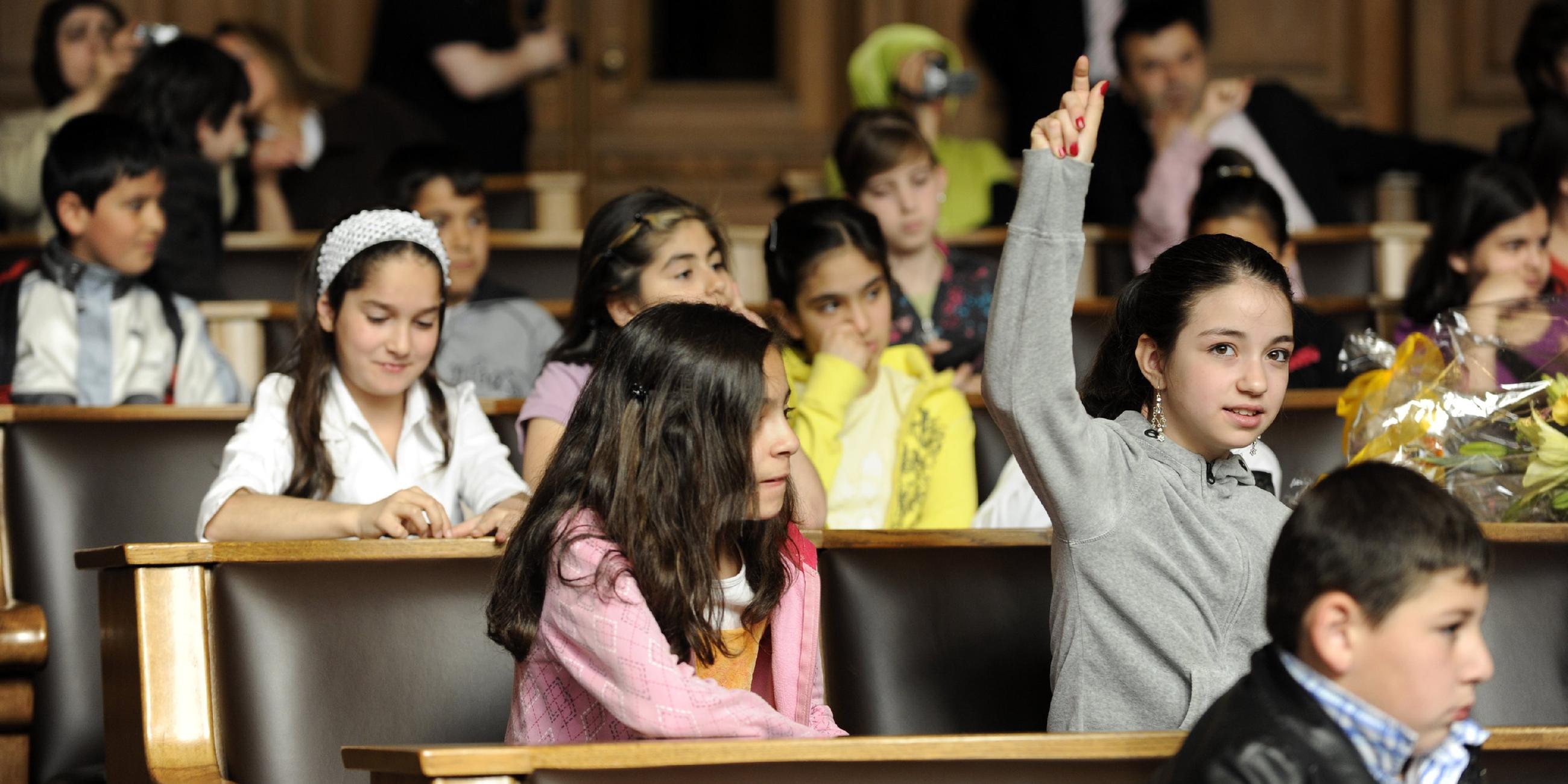 Kinder sitzen nebeneinander und melden sich