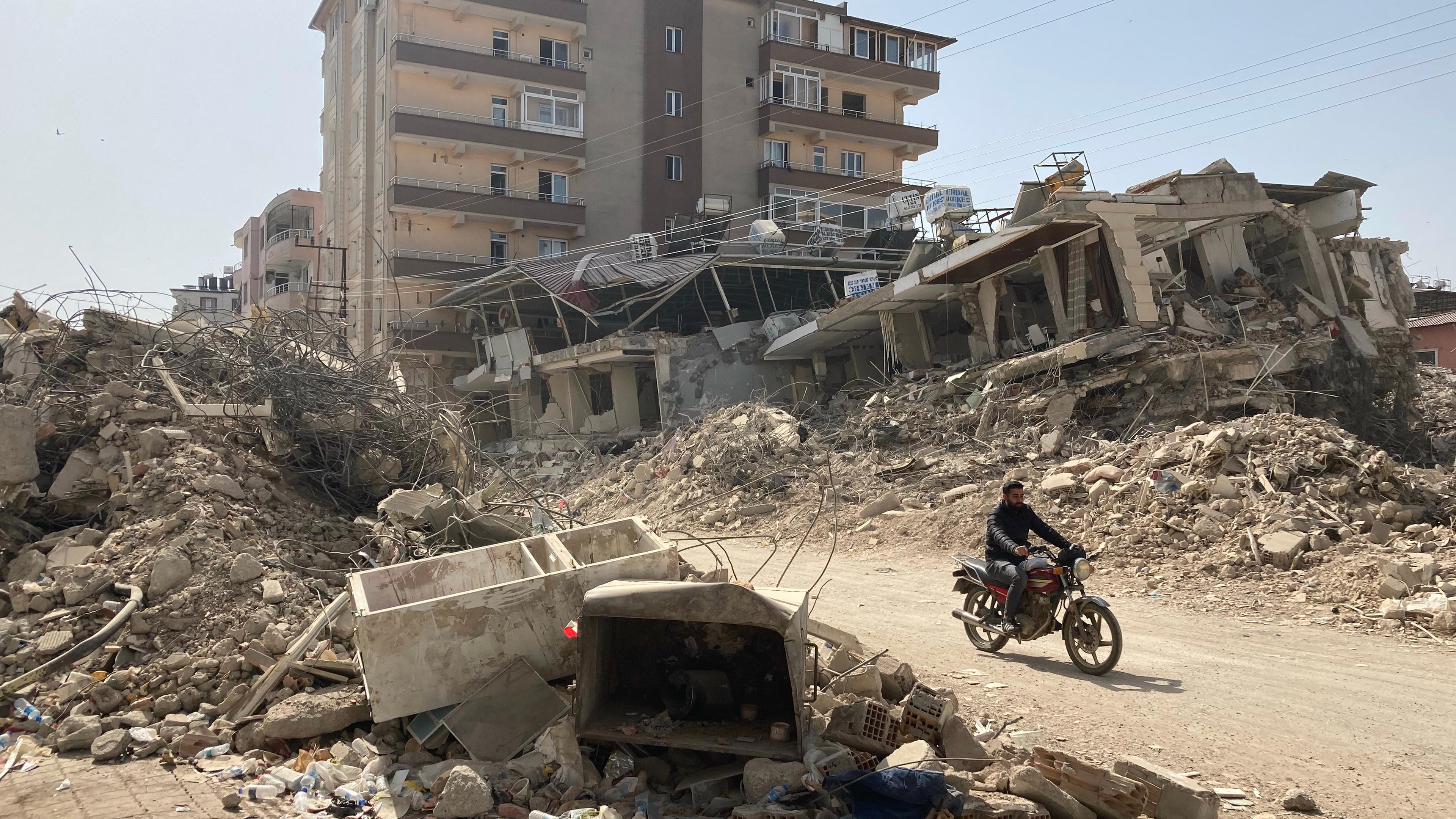 Türkei, Kirikhan: Ein Mann fährt auf einem Motorrad zwischen zerstörten Häusern im türkischen Ort Kirikhan nahe der syrischen Grenze hindurch.