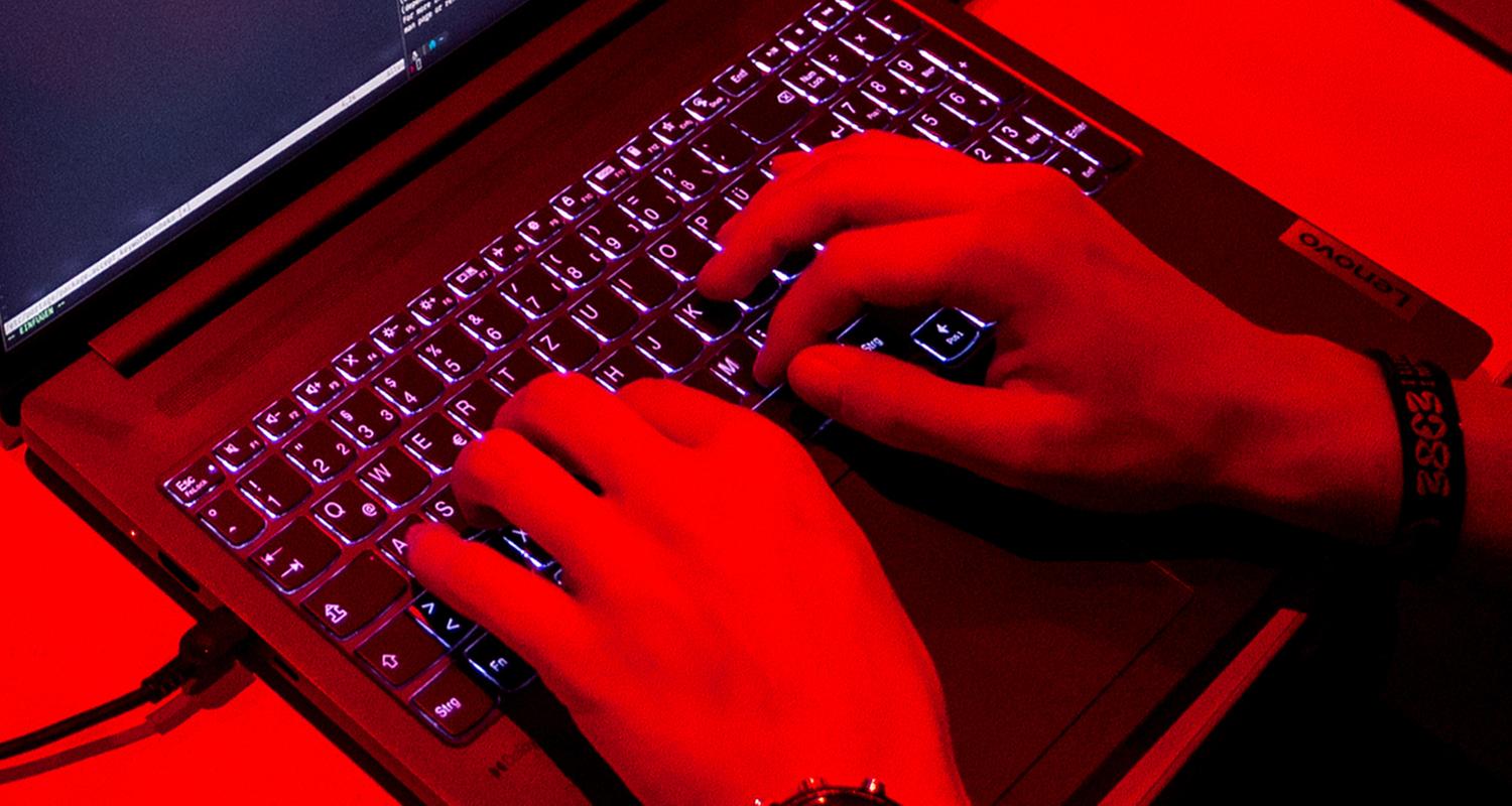 Hände tippen in rotem Licht auf einer Laptop-Tastatur (Typical Hacker-Angriffe)