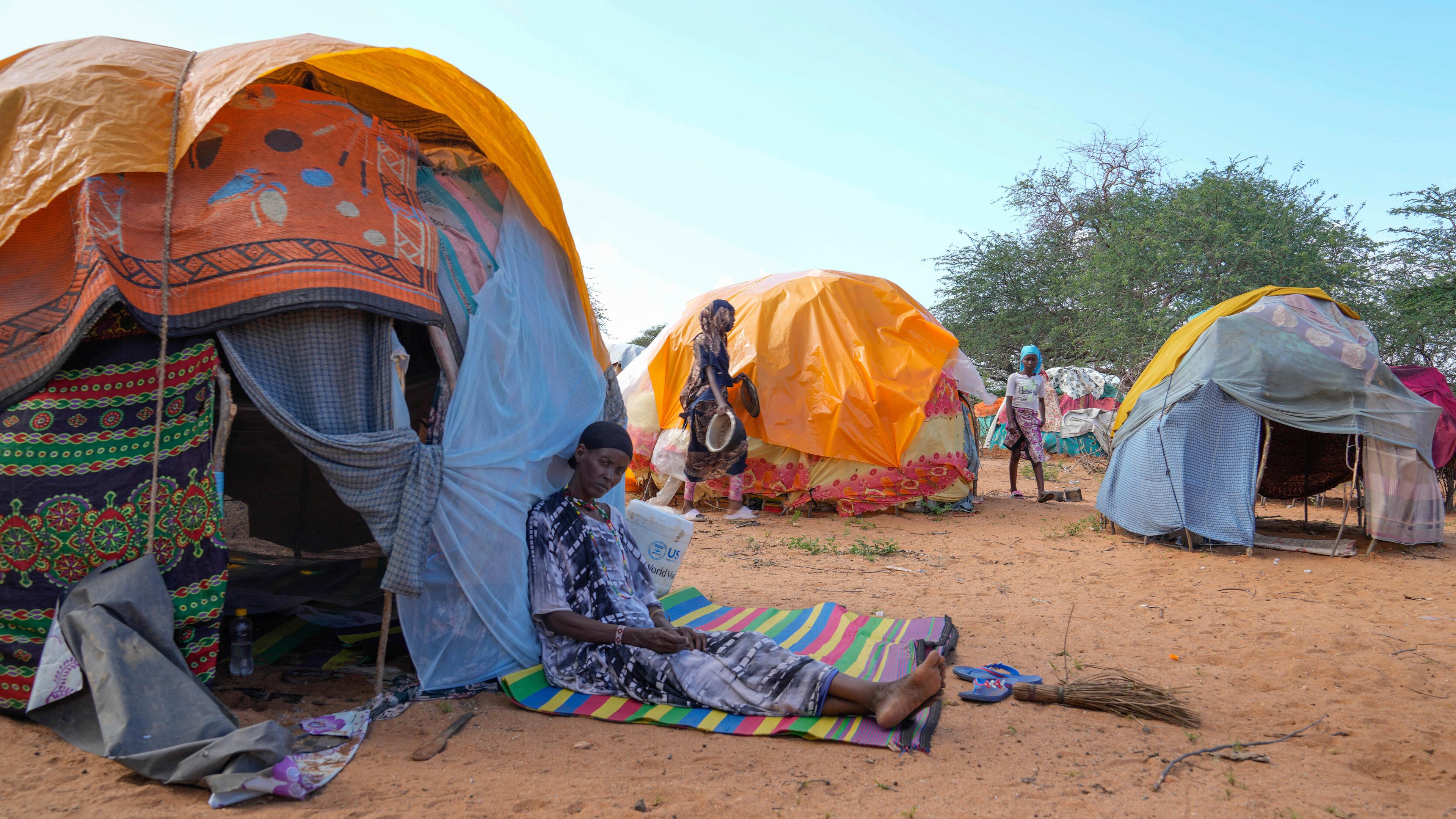 Eine Person sitzt vor einem provisorischem Zelt in einem Vertriebenenlager.