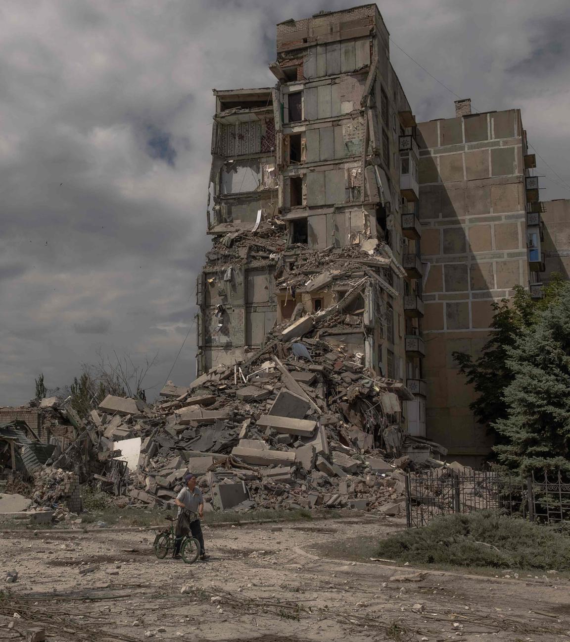 Ein Einwohner von Torestsk in der Ukraine schiebt ein Fahrrad an einem zerstörten Gebäude vorbei.