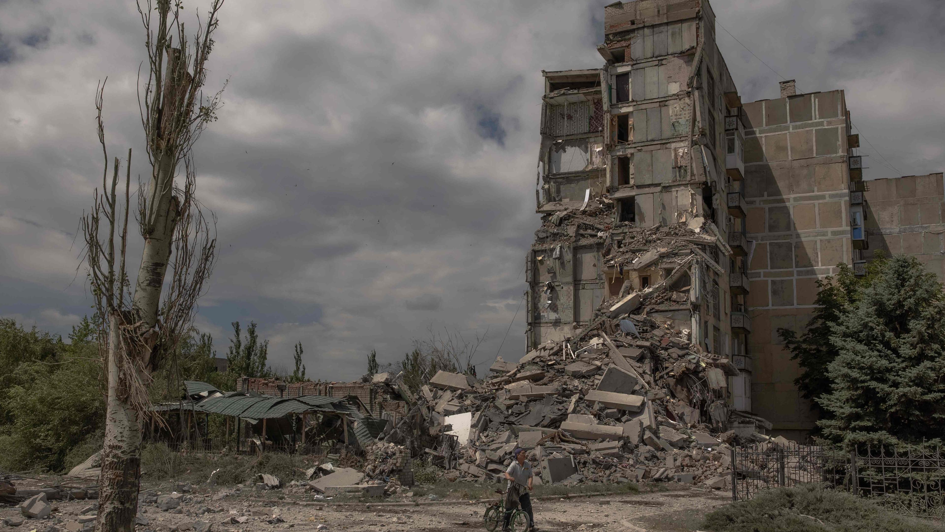 Ein Einwohner von Torestsk in der Ukraine schiebt ein Fahrrad an einem zerstörten Gebäude vorbei.