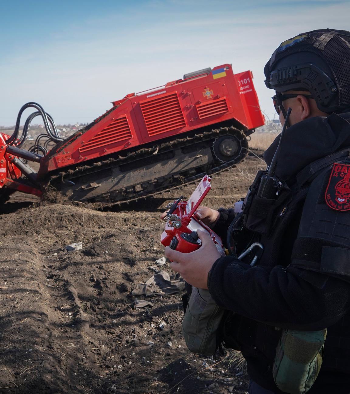 Ein Soldat bedient ein rotes Gerät zur Minenräumung auf einem Feld.