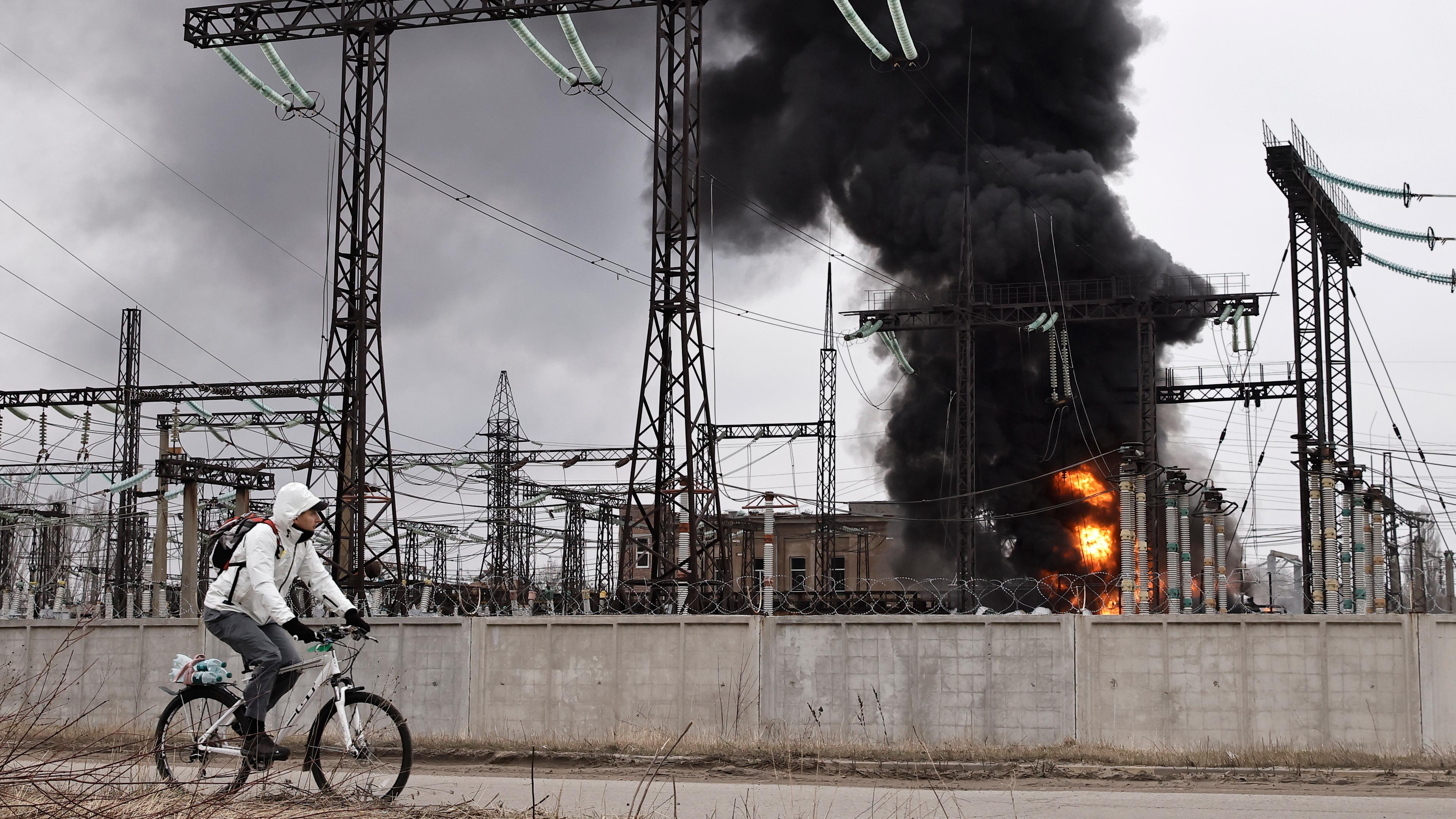 Ein Mann radelt nach einem russischen Angriff an einem Elektrizitätswerk vorbei. Dort ist ein Feuer ausgebrochen.