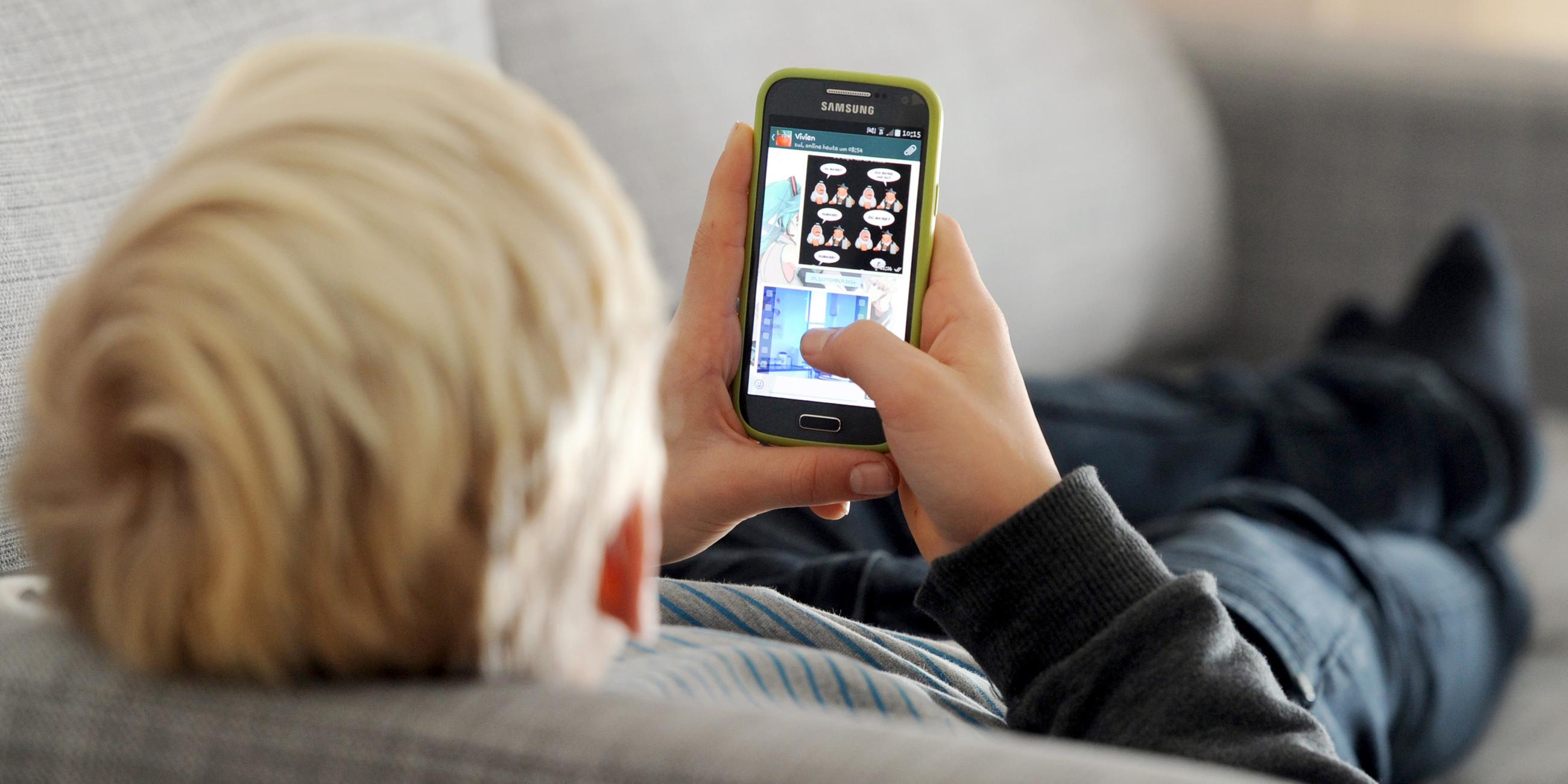  Ein Kind liegt auf einem Sofa und blickt auf sein Smartphone. Kinder in reichen Ländern produzieren viel Elektroschrott. 