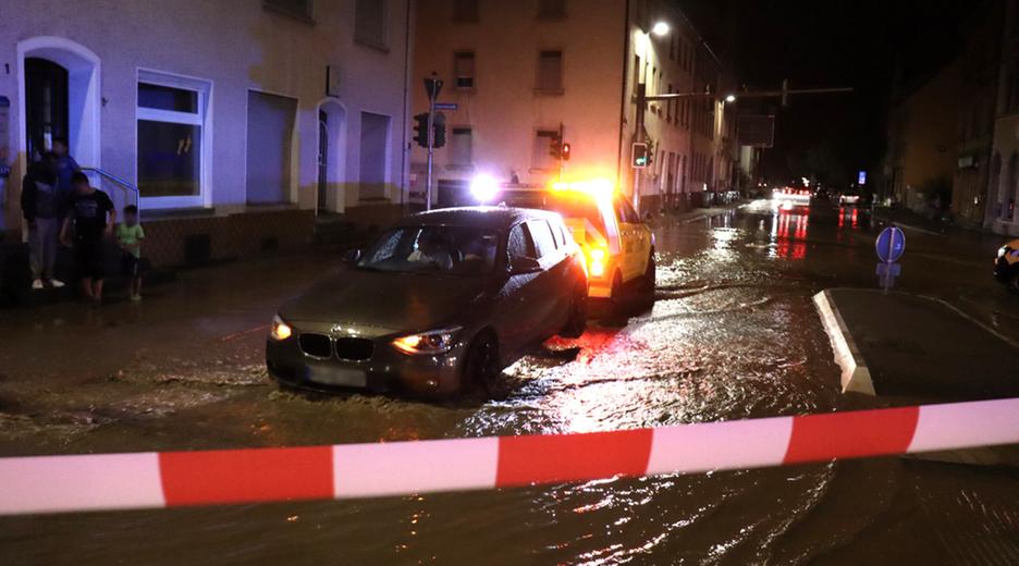 13.08.2024, Baden-Württemberg, Landkreis Karlsruhe: Hochwasser überflutet im Landkreis Karlsruhe eine Straße während ein Auto abgeschleppt wird.