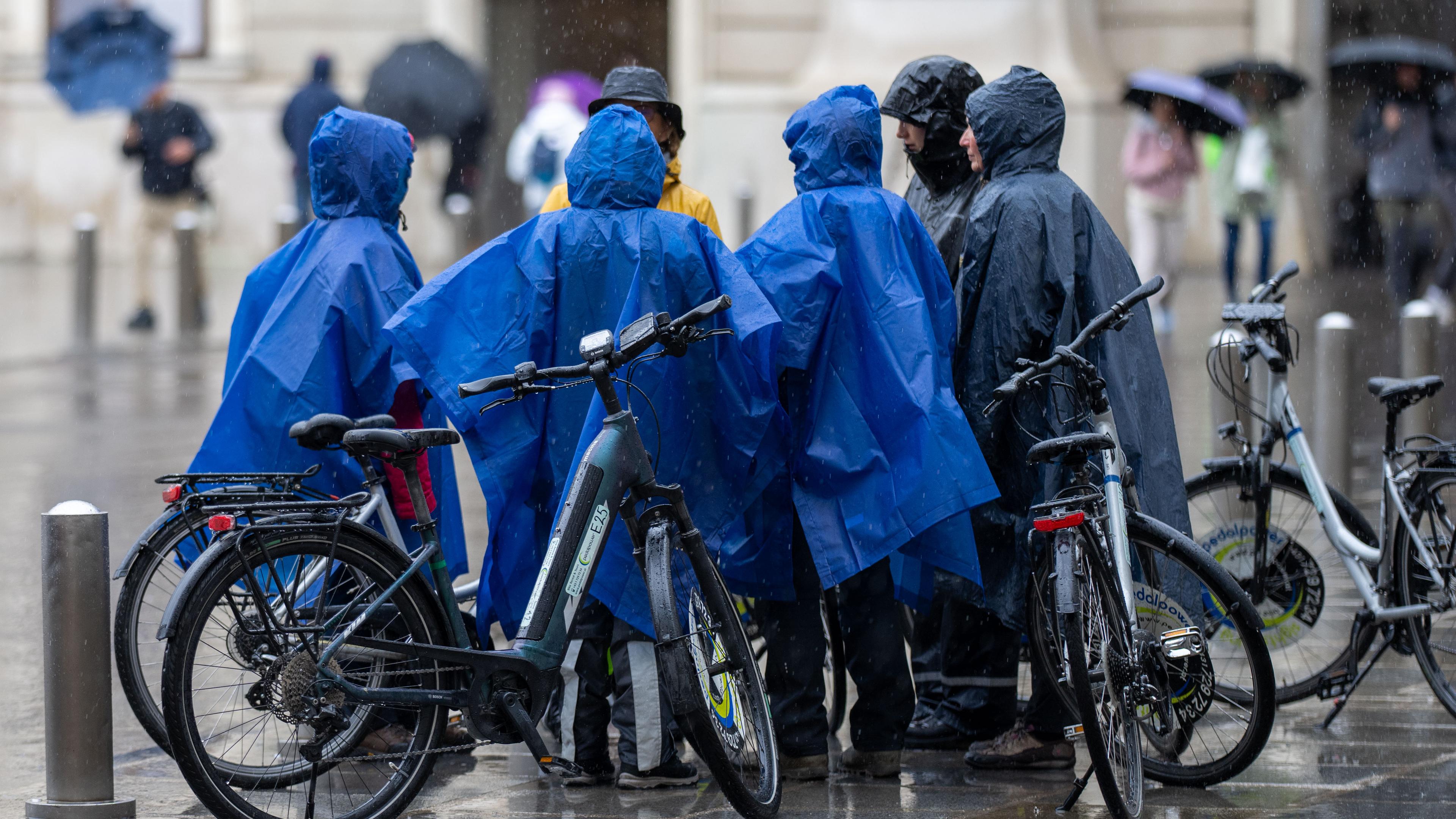 Österreich, Wien: Menschen schützen sich im Regenmänteln vor dem Regen. 