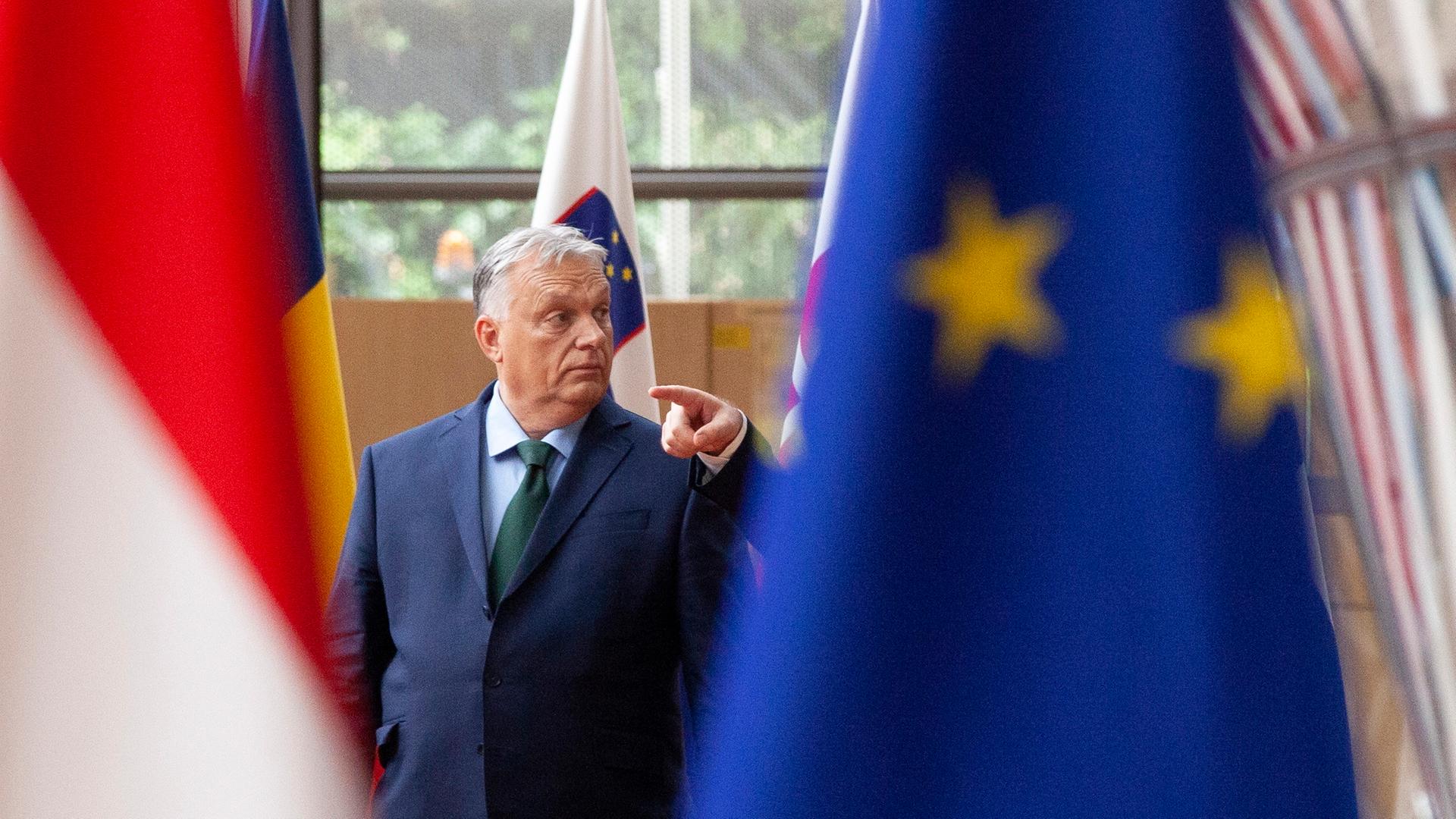 Hinter der ungarischen Flagge und der europäischen steht Victor Orban im dunklen Anzug.
