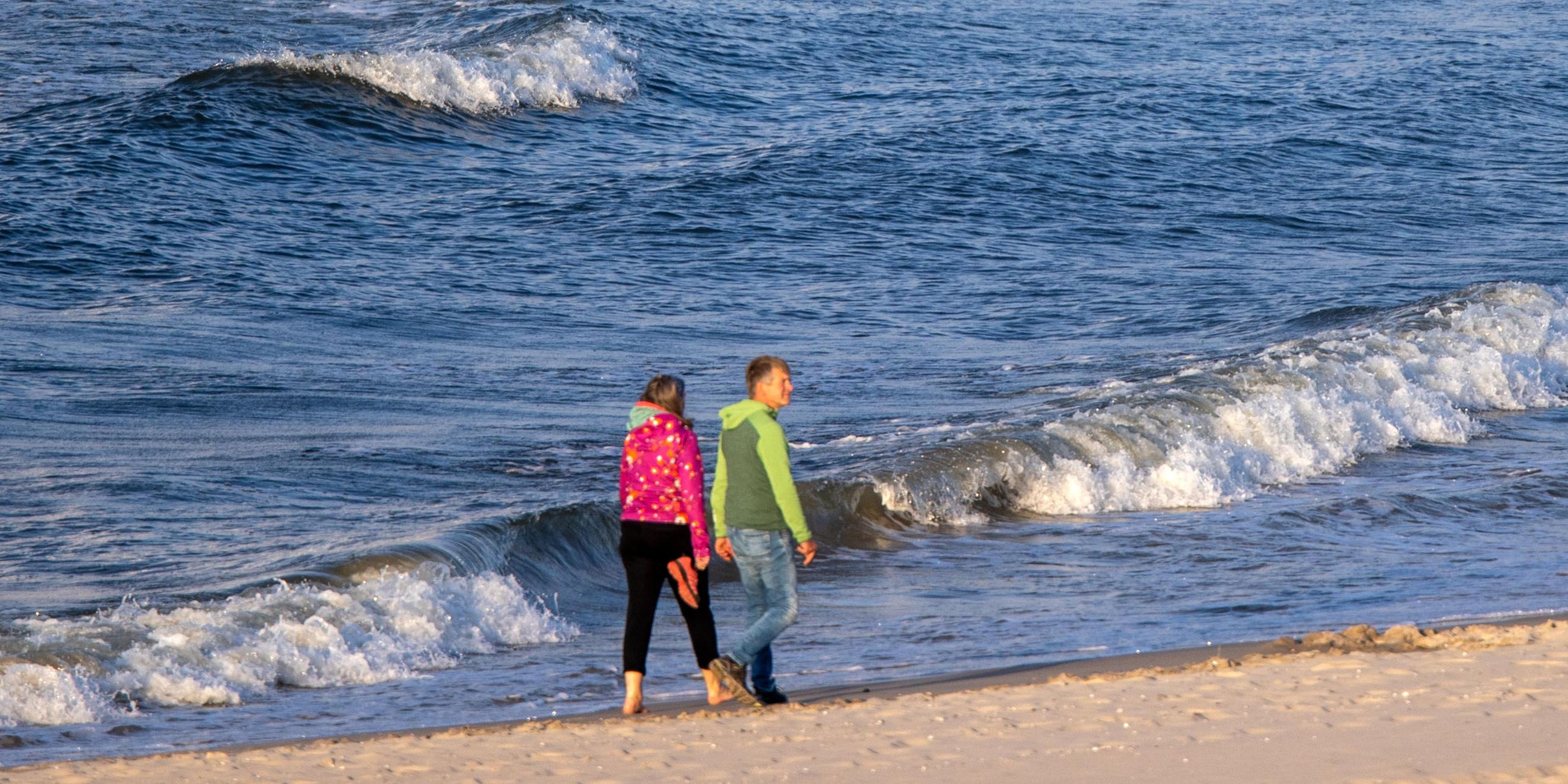 Spaziergänger gehen bei starkem Wind und kräftigem Wellengang auf der Ostsee am Strand der Insel Usedom am 12.06.2021 entlang.