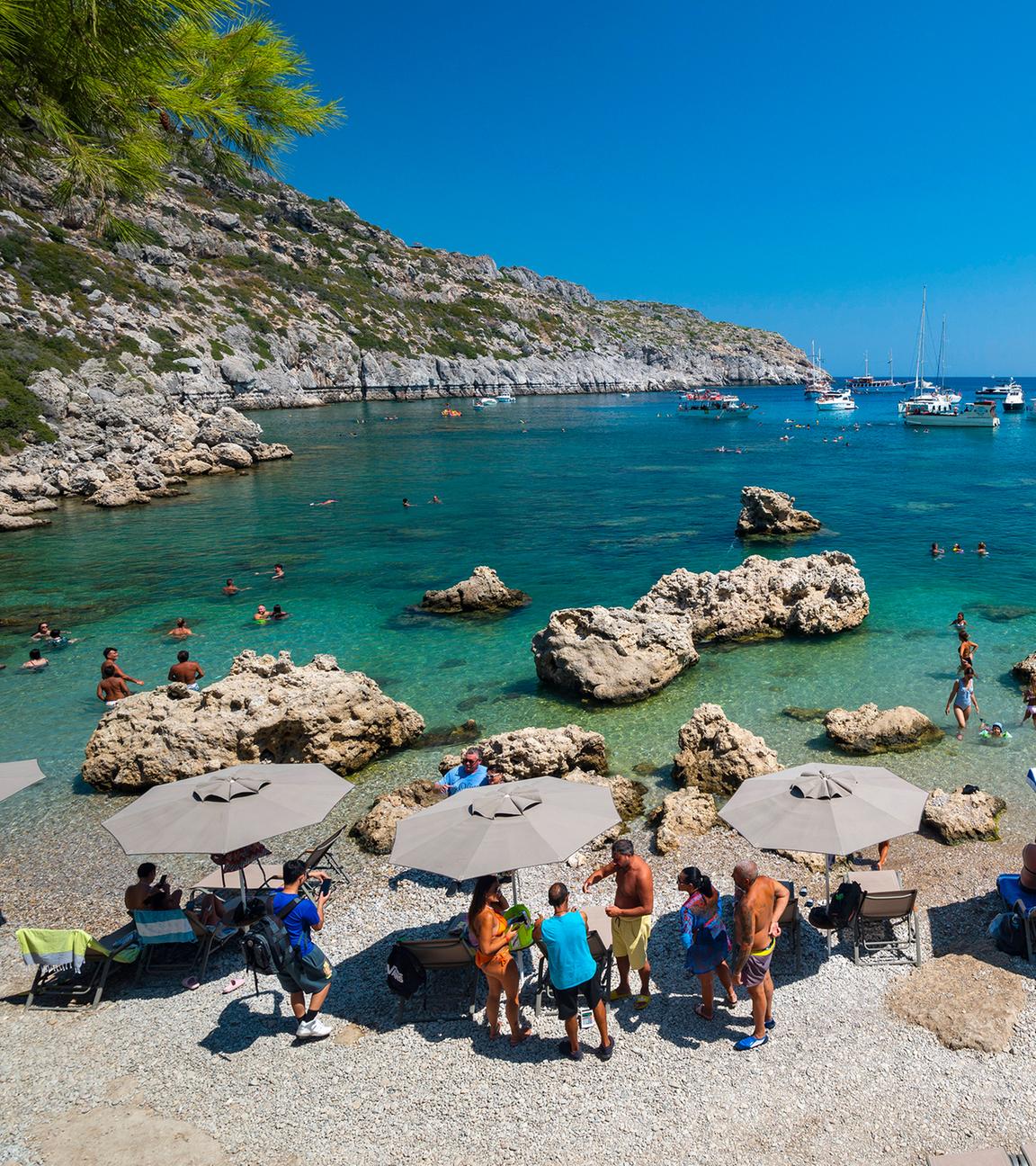 Touristen unter Sonnenschirmen am Strand von Rhodos