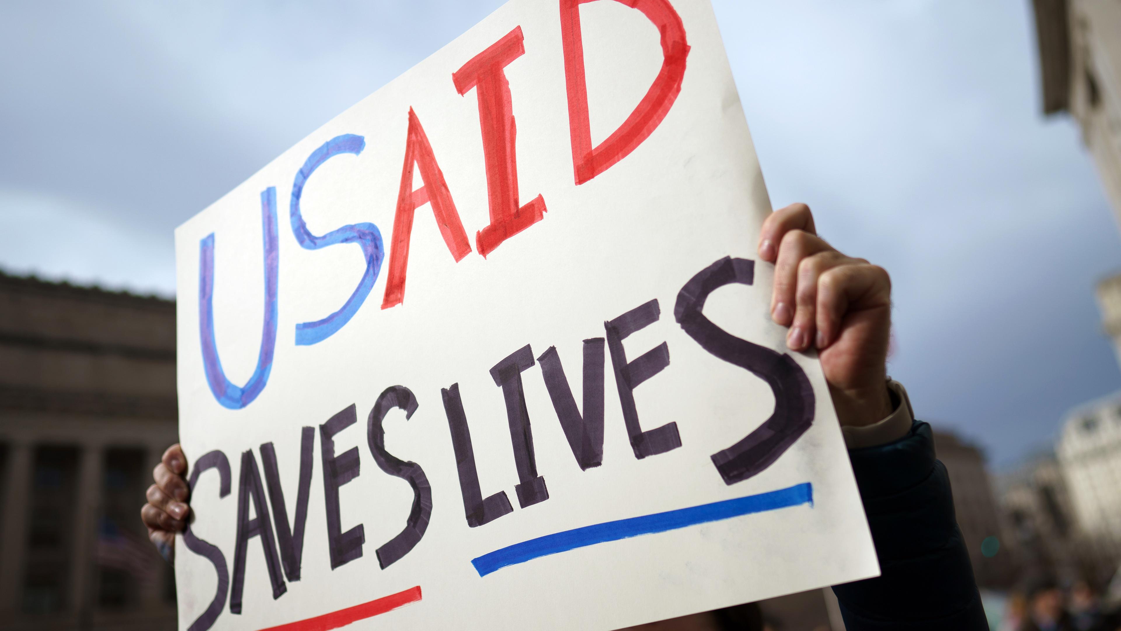 Demonstrant hält Schild mit der Aufschrift "USAID safes lives".